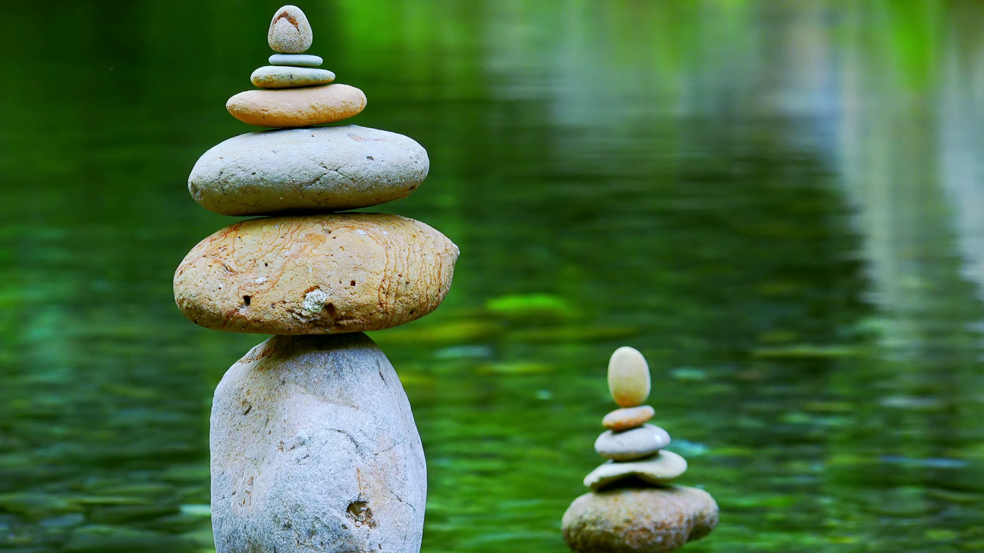 videoblocks-close-up-shot-of-rocks-stacked-on-top-of-each-other-and-placed-in-quiet-jungle-lake-meditation-scene-with-stone-piles-by-side-of-water-symbol-of-balance-harmony-and-tranquility-camera-stays-still_s6uptyxyz_.png