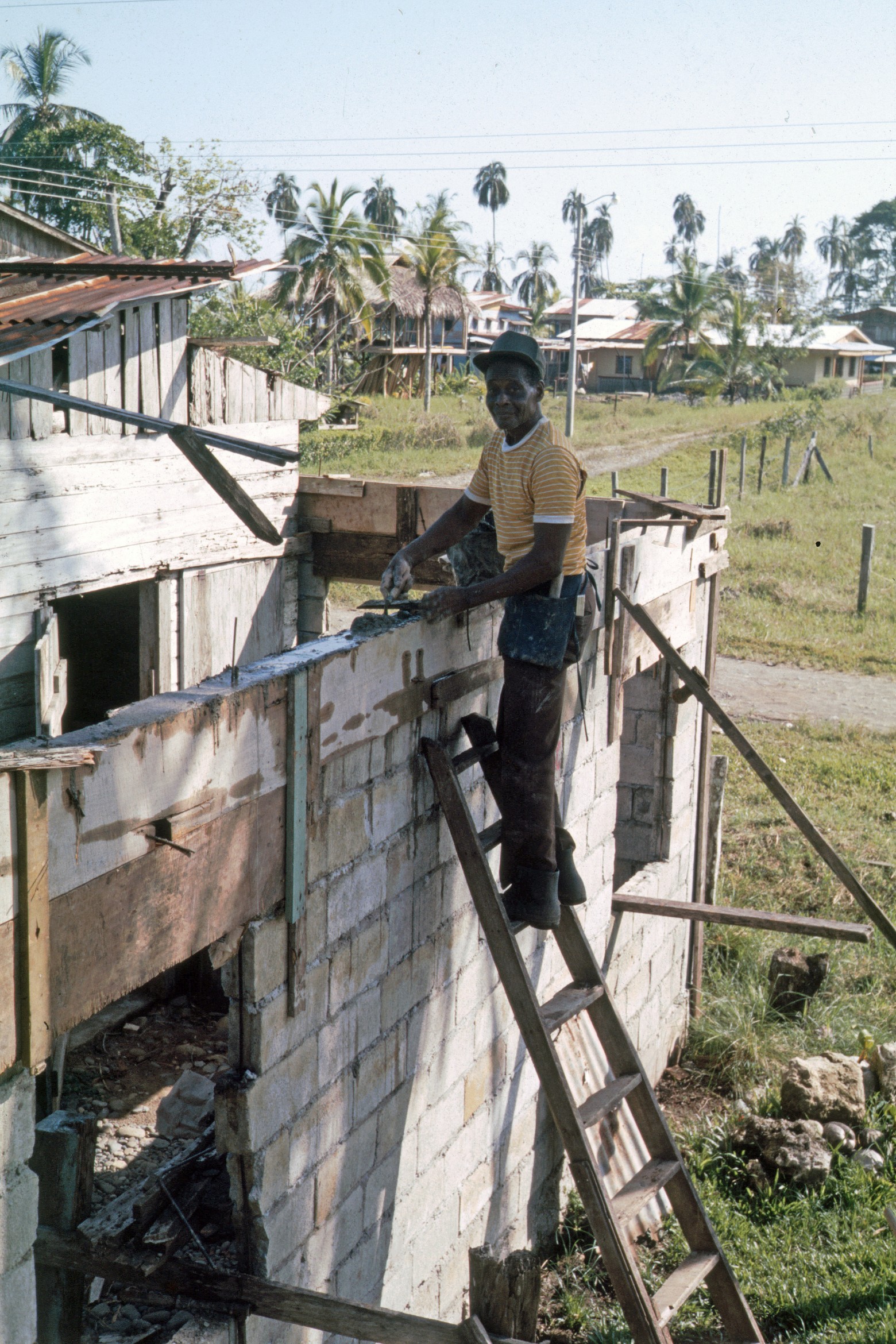   Mr. Patterson Construyendo    Puerto Viejo    1986    Mr. Patterson construyendo con cemento nueva casa alrededor de casa vieja de madera en el fondo casa de Aldo en consrucción con techo de hojas    CZ_001_010  