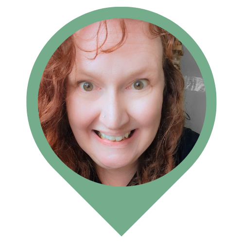 A close selfie of a smiling woman with red curly hair.