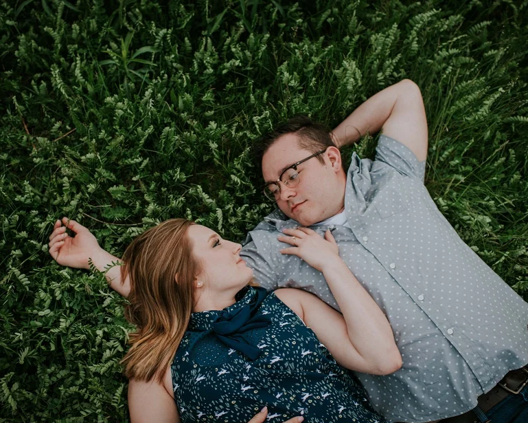 A man and woman lying on grass, facing each other, appearing to have a romantic moment.