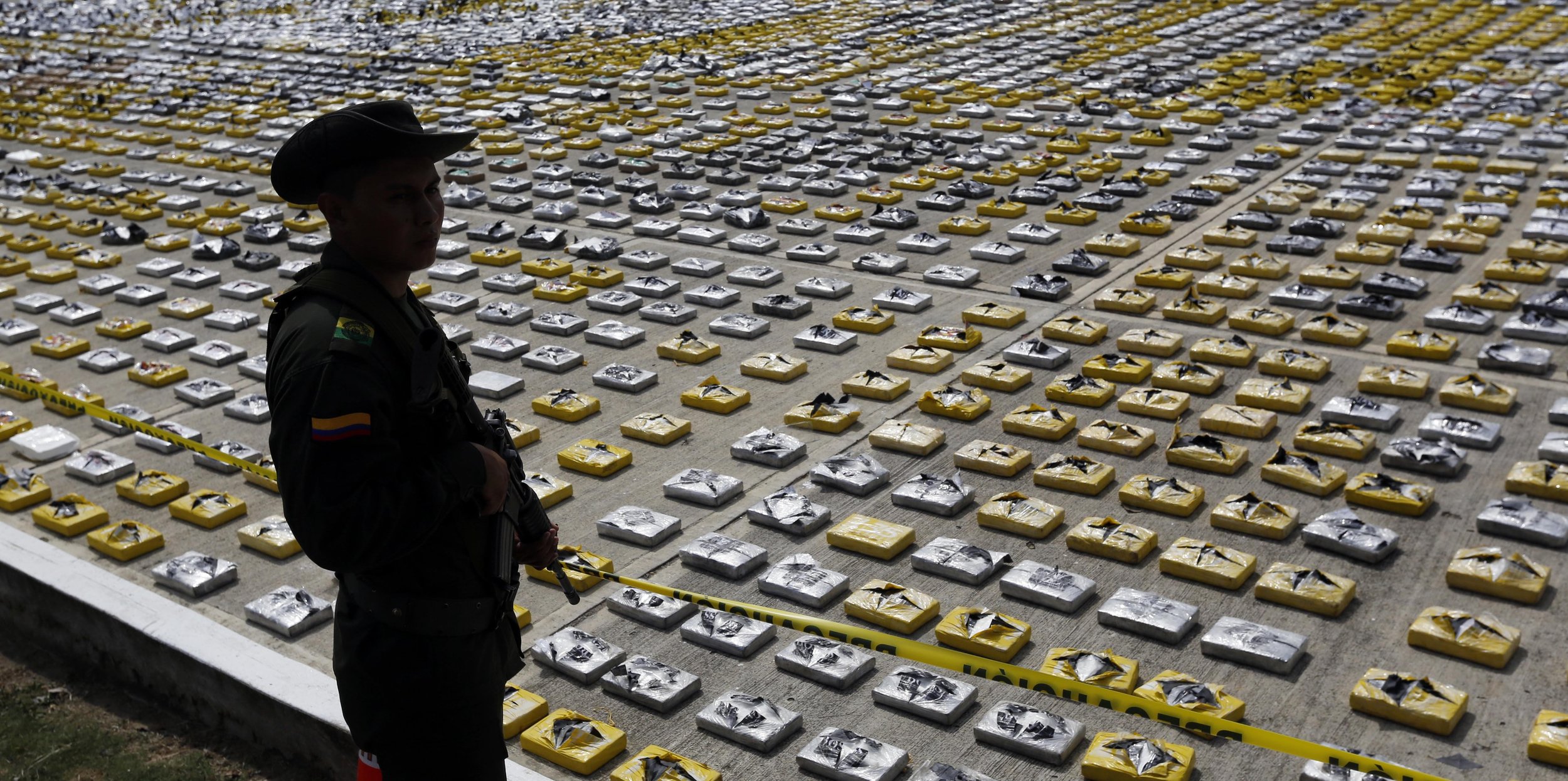 An armed police officer stands guarding packages of seized cocaine in Colombia, 2015