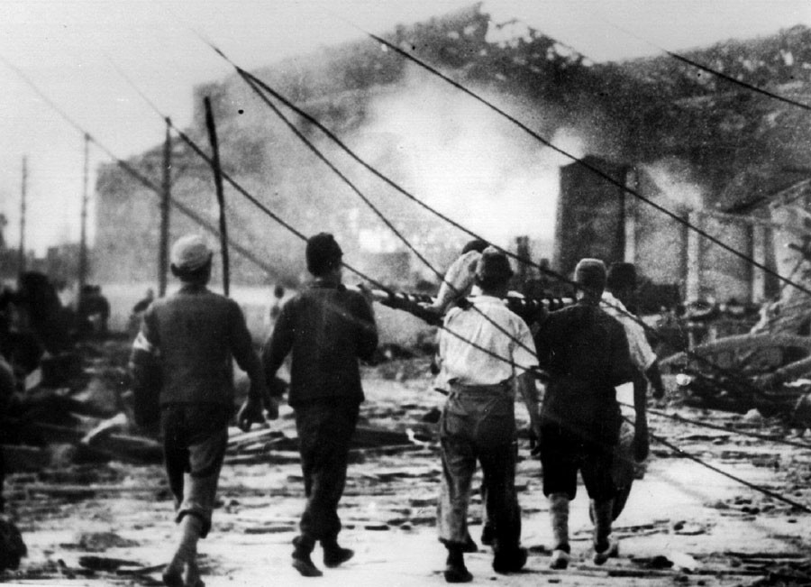 Japanese air raid workers carry a victim of the atomic bomb in Hiroshima away from smoking ruins on 6th August 1945. Photo source: Reuters.