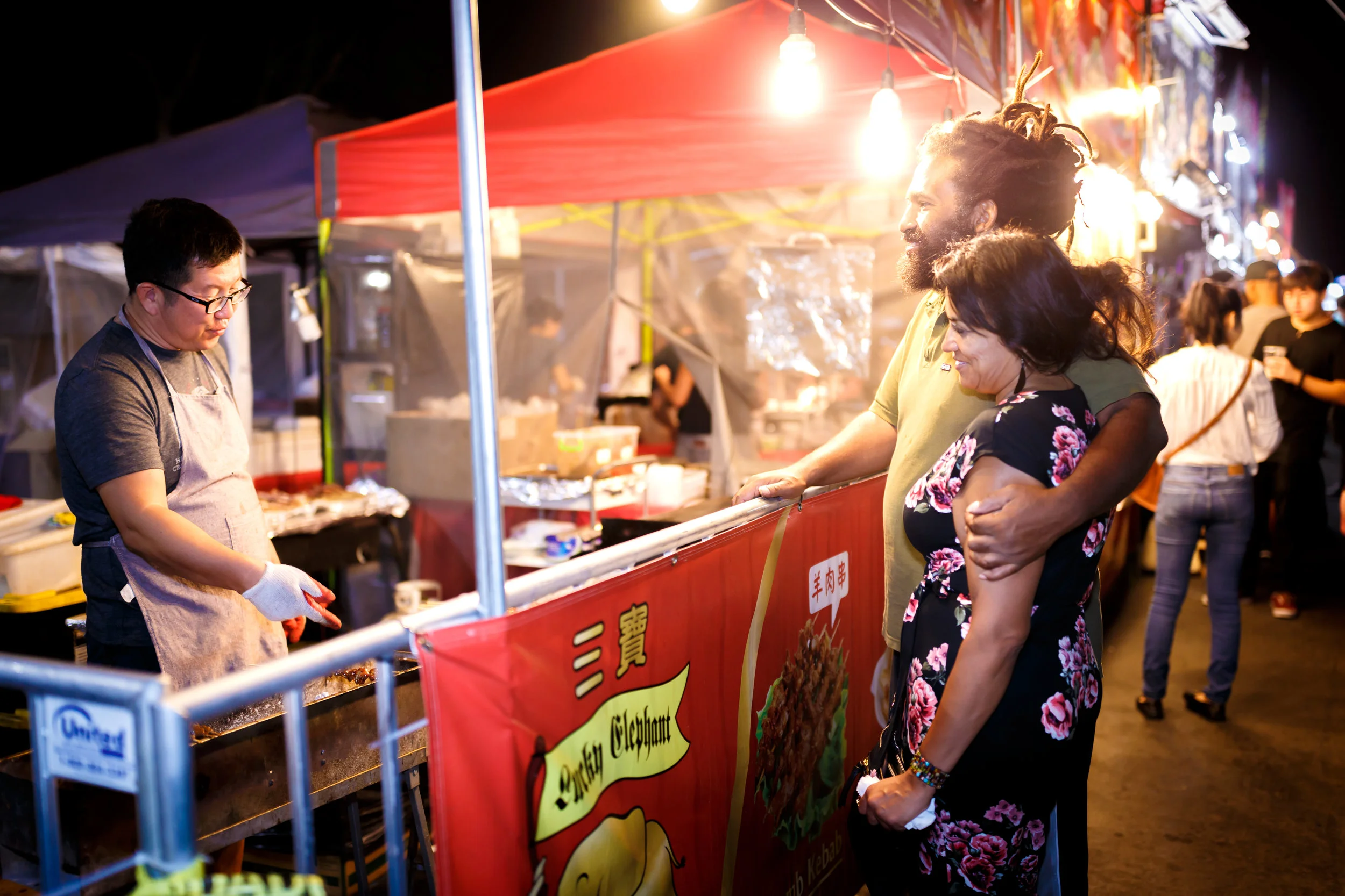A cute couple watches vendor Lucky Elephant grill some tasty street snacks. Photo by John Truong.