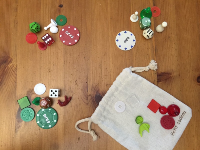 Grab Bag showing player poker chips with betting on them, and their respective collected tokens (which shows Red and Green tied as winners of the Grab, with 7 tokens each), and the results in the bag as the leftover tokens (which shows that Red wins the Bag)