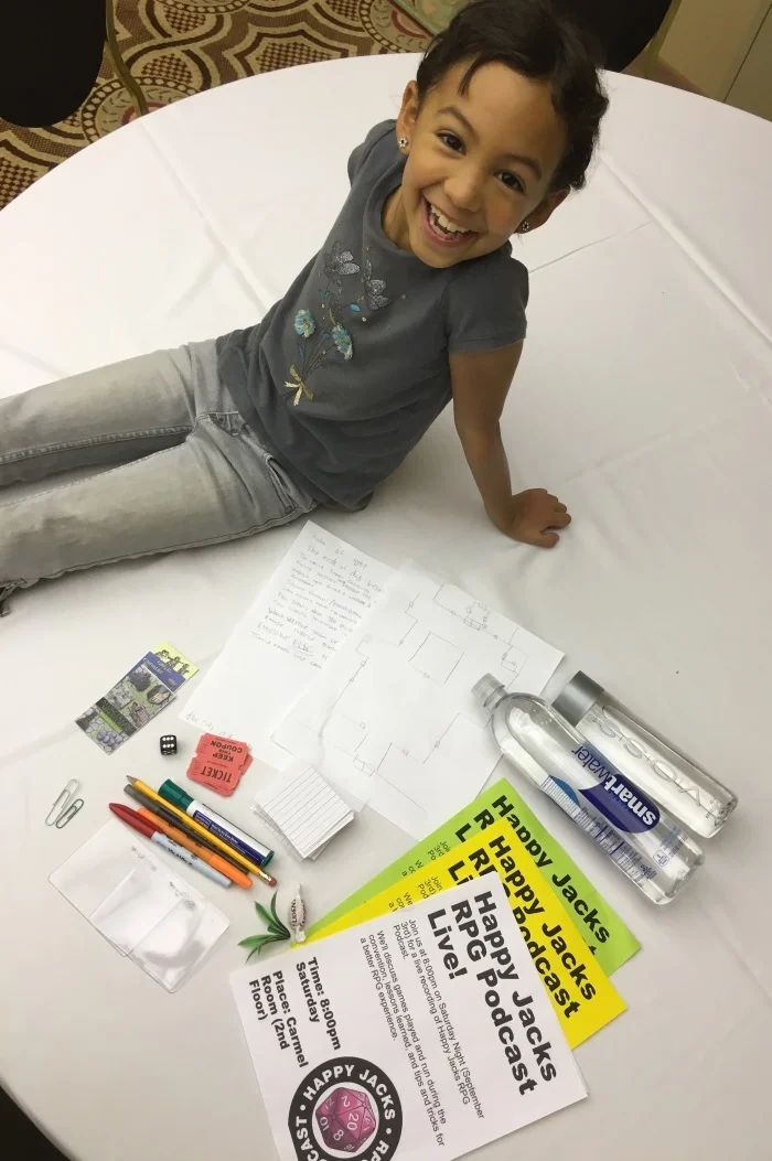 Nova with her finds... writing tools, unused tickets, paper clips, empty badges, Happy Jacks flyers in 3 flavors, 10 cents CRV, a map, and the holy grail: a die.