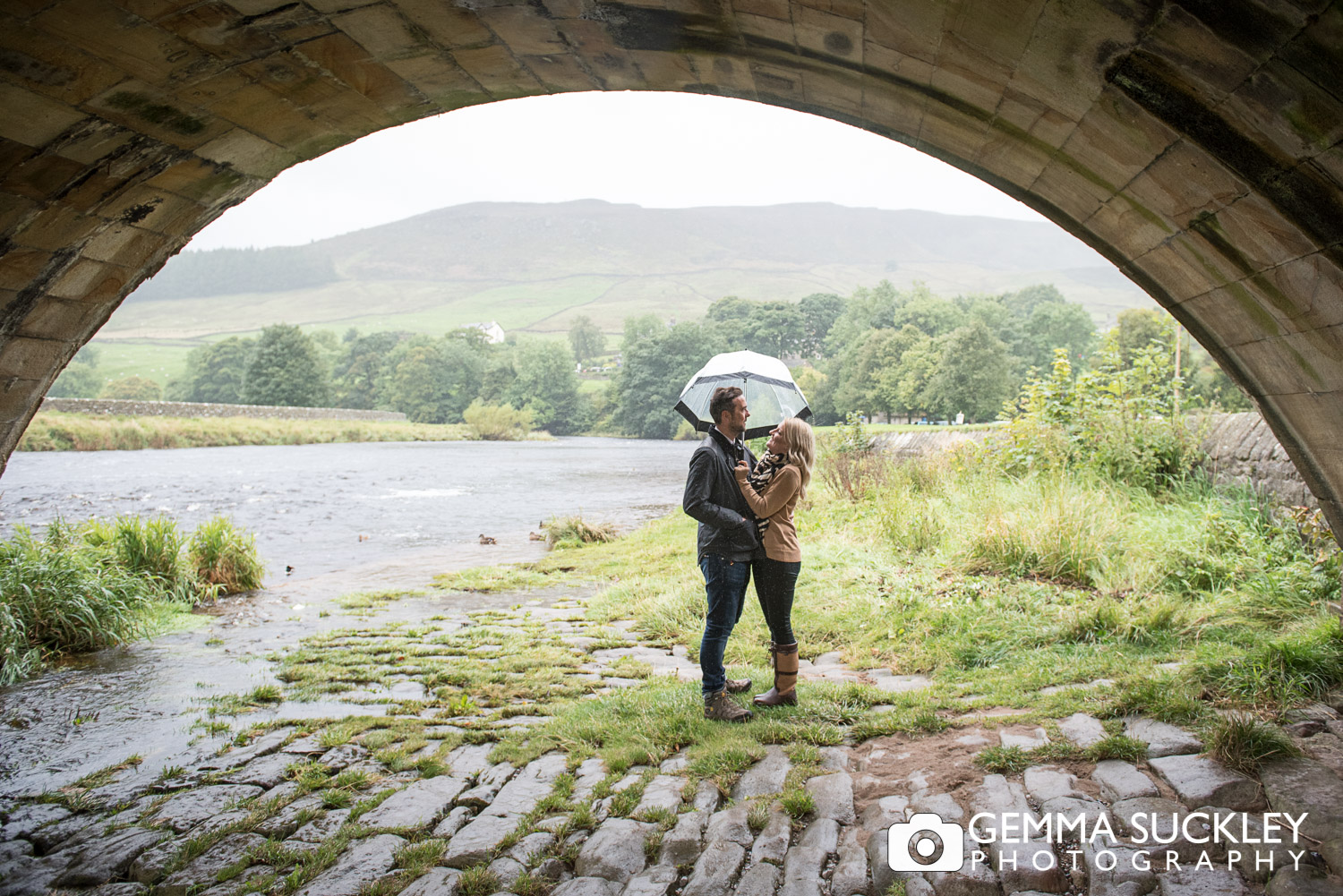 couple with an umbrella under burnsall bridge