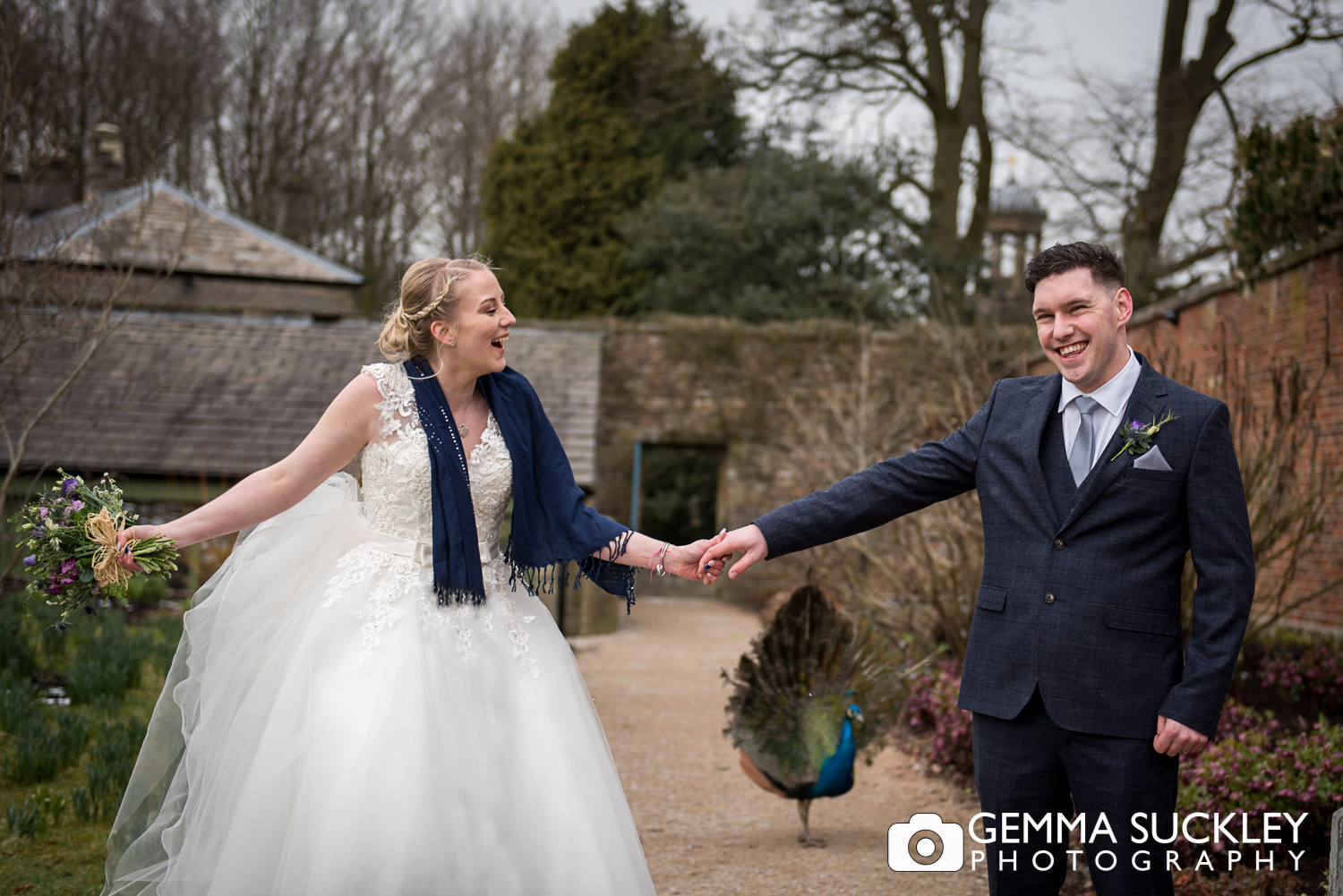bride and groom at broughton hall with a peacock behind them 