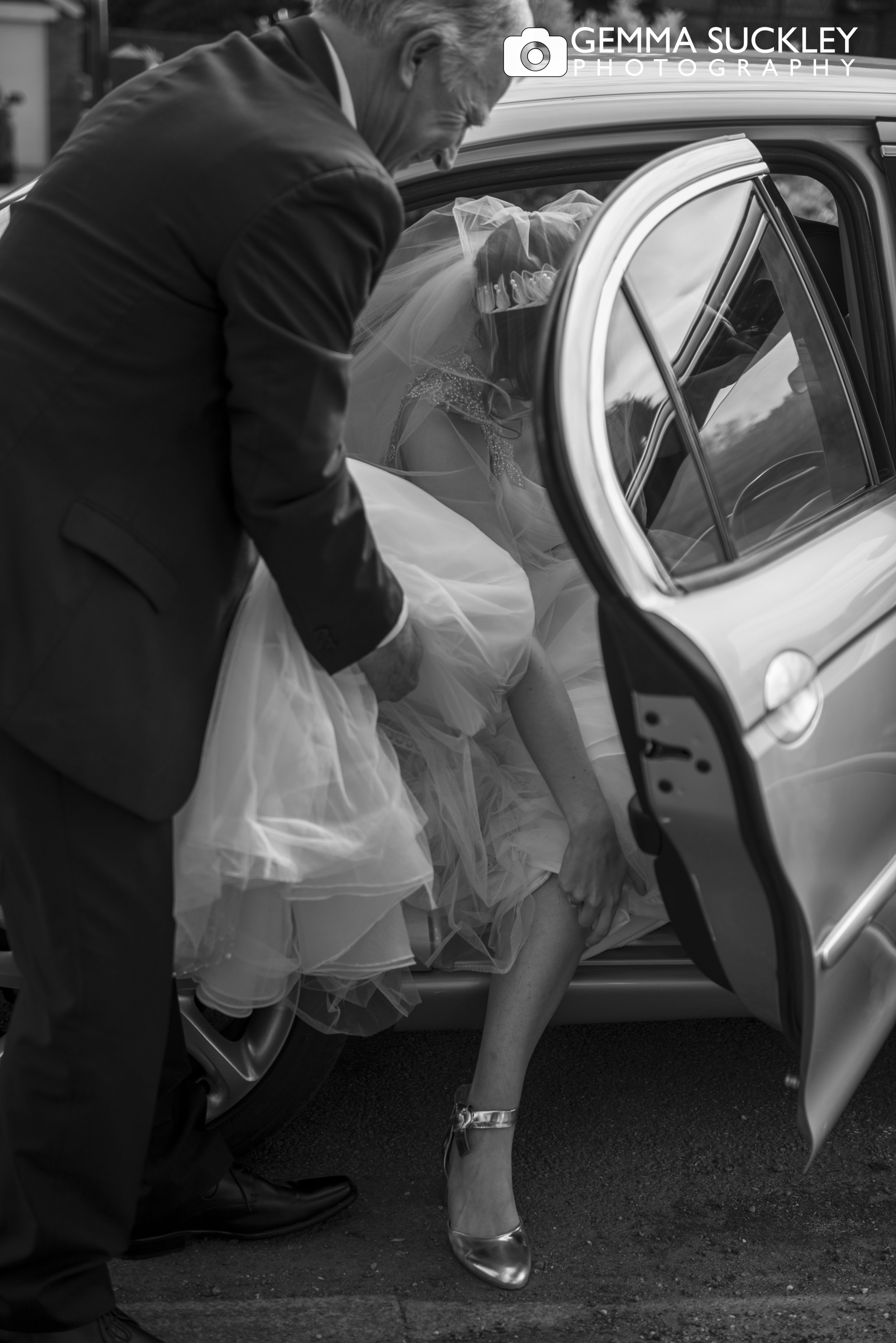 black and white photo of bride getting out of the car on arrival to the church