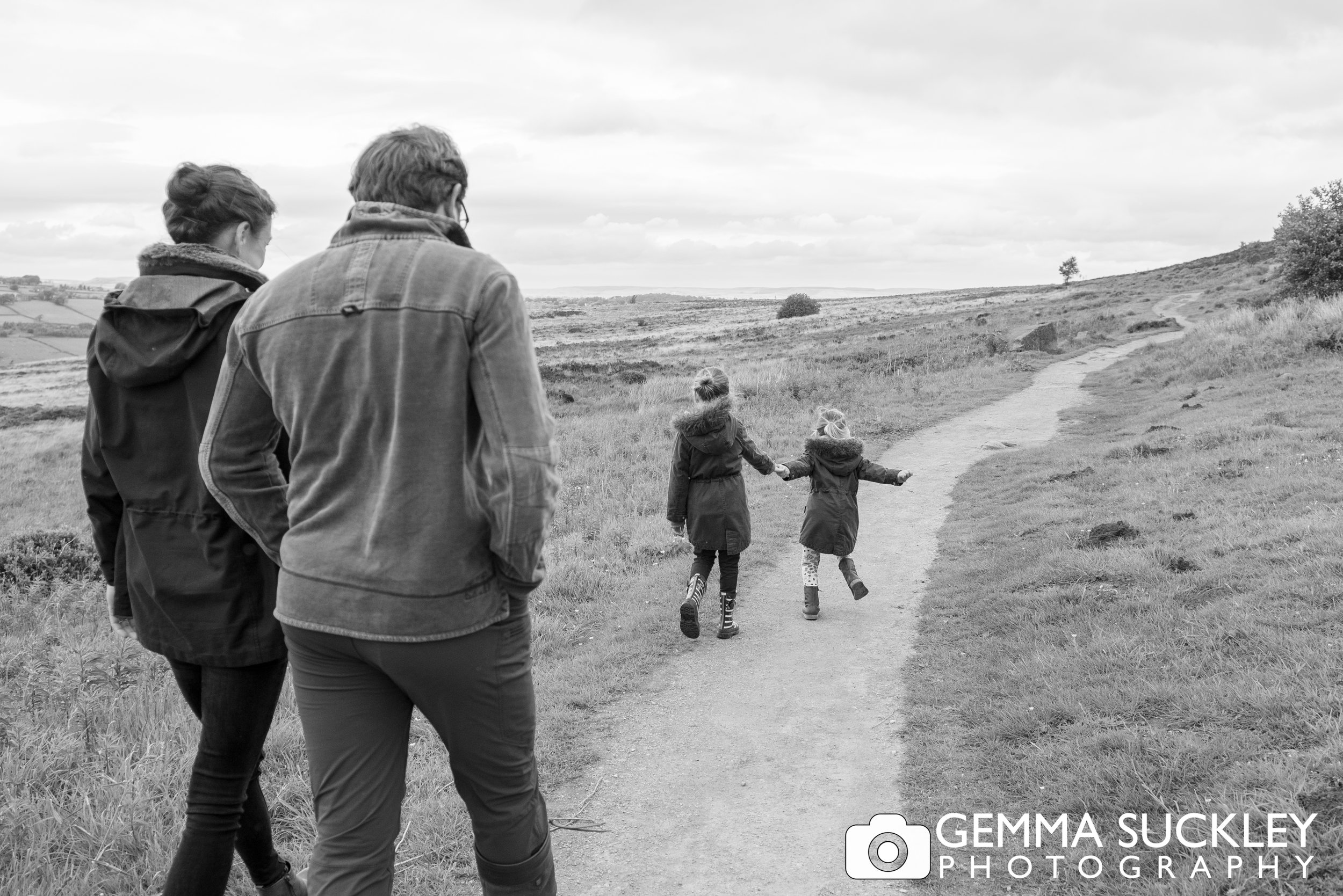 black and white photo, naturally capturing a mum ans dad walking with their kids running ahead 