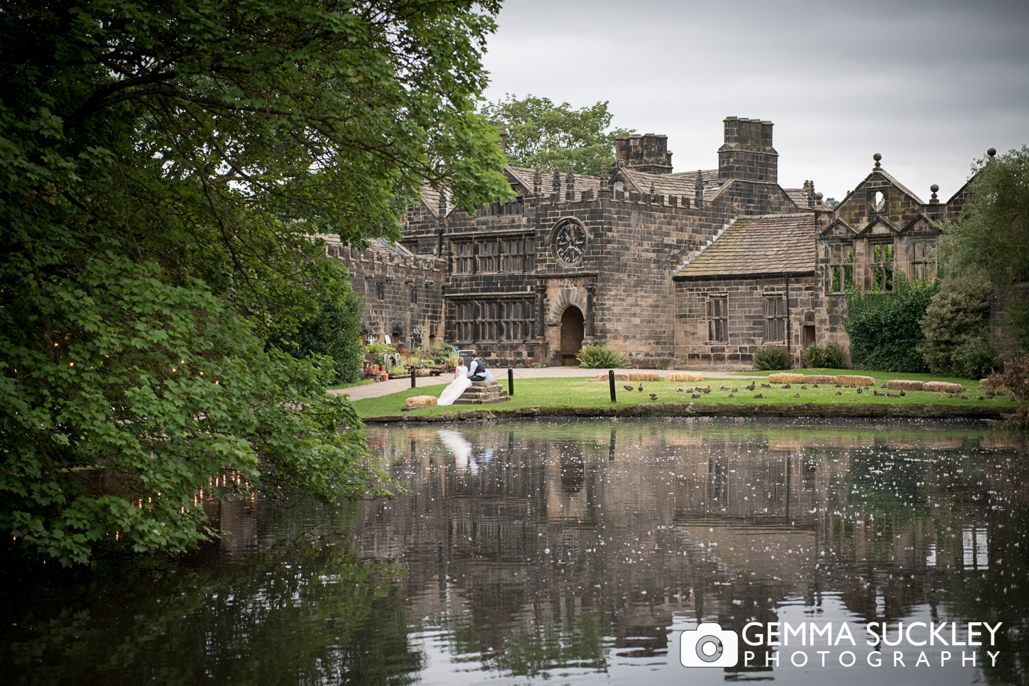 view of the pond and east riddlesden gall with the bride and groom in the distance