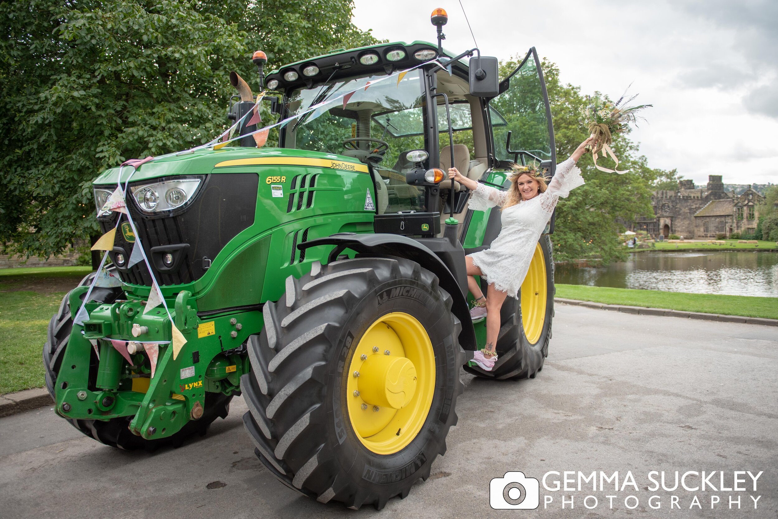 a bride climbing on a tractor with east riddlesden hall in the background