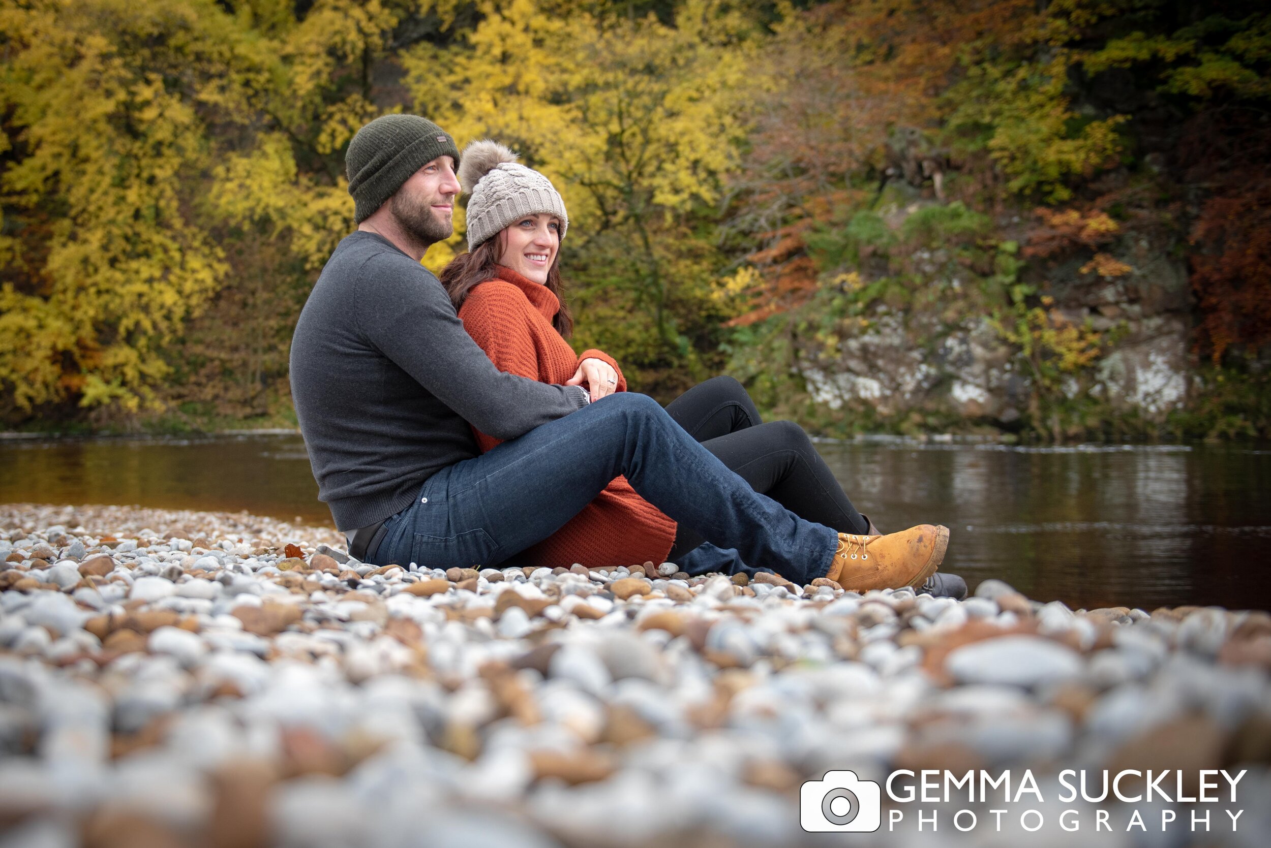 an autumnal photo of a couple sat by the river at bolton abbey