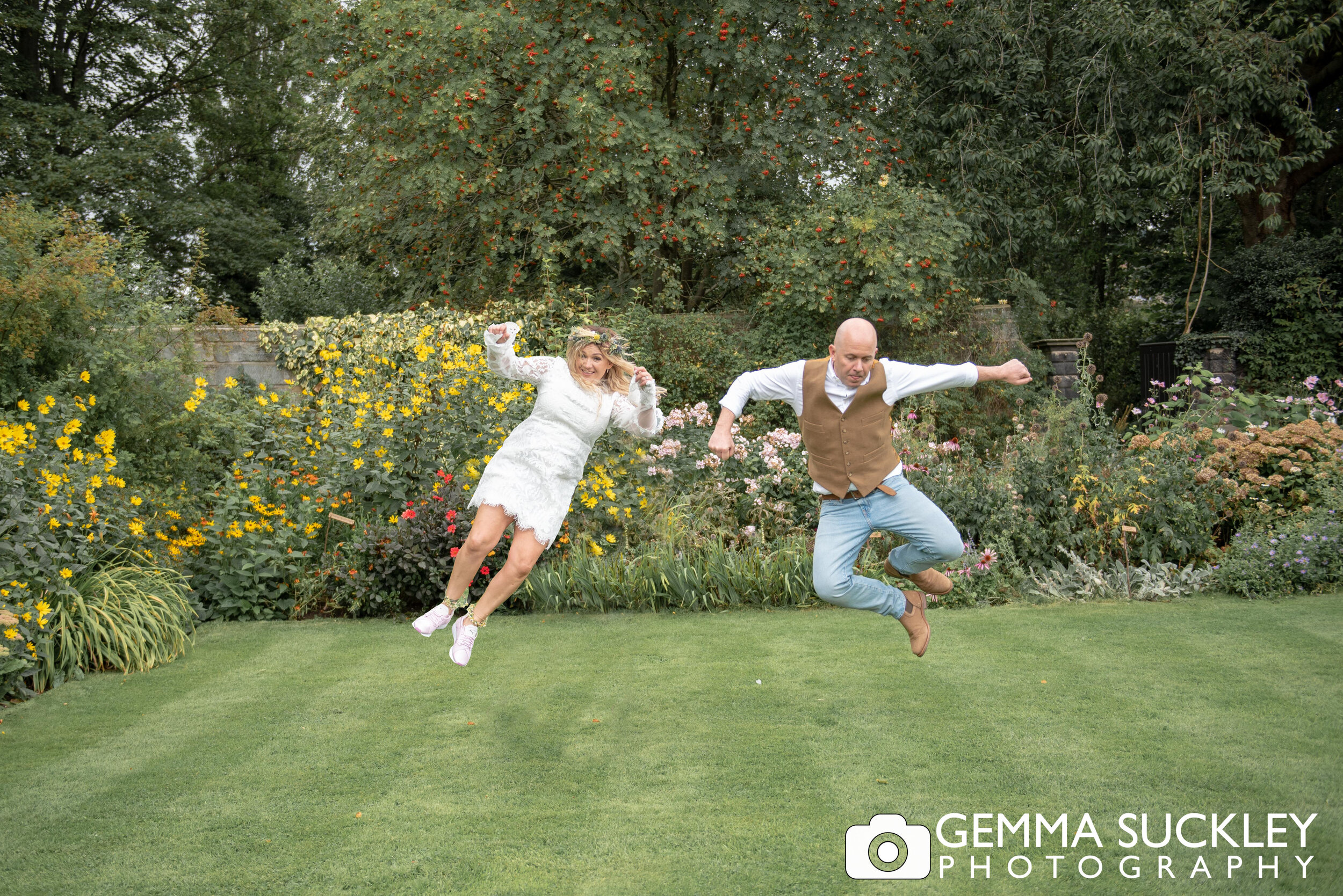 bride and groom jumping in the air in the gardens at east riddlesden hall