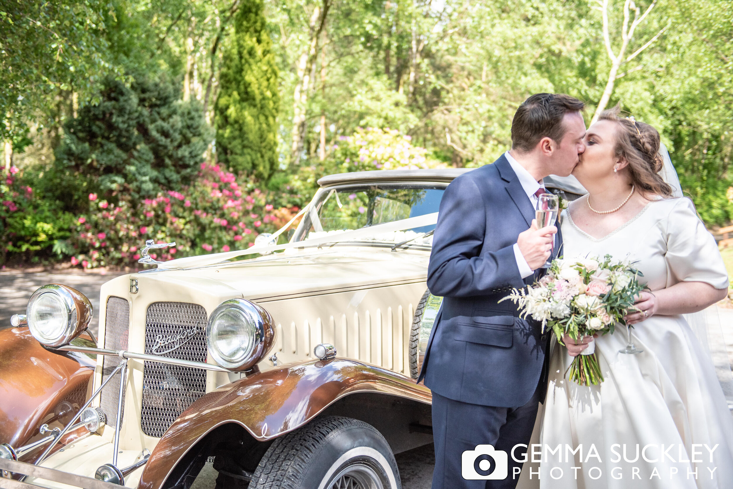 bride and groom kissing next to their wedding car