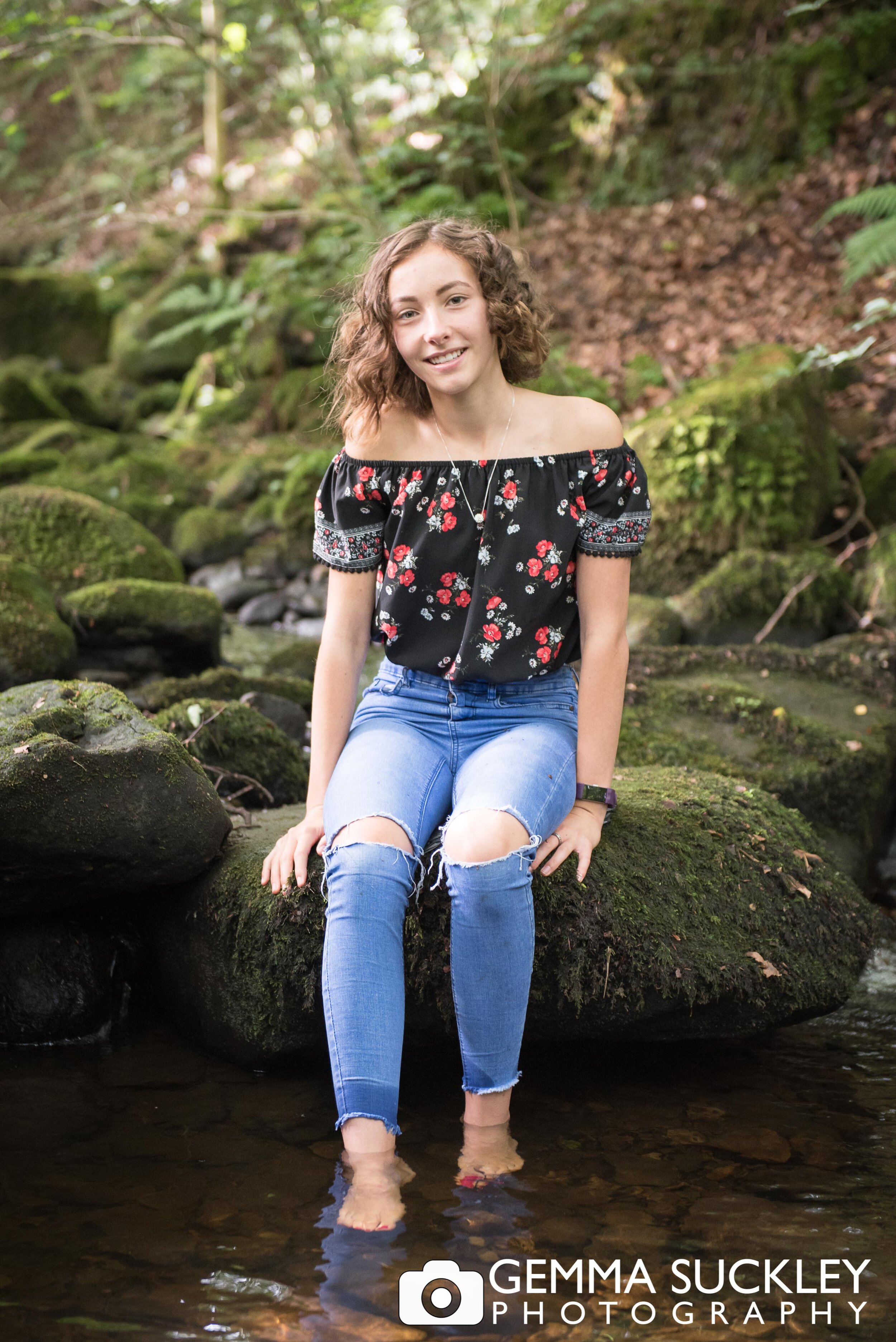 teenager smiling for a photo shoot while she dips her feet into the river