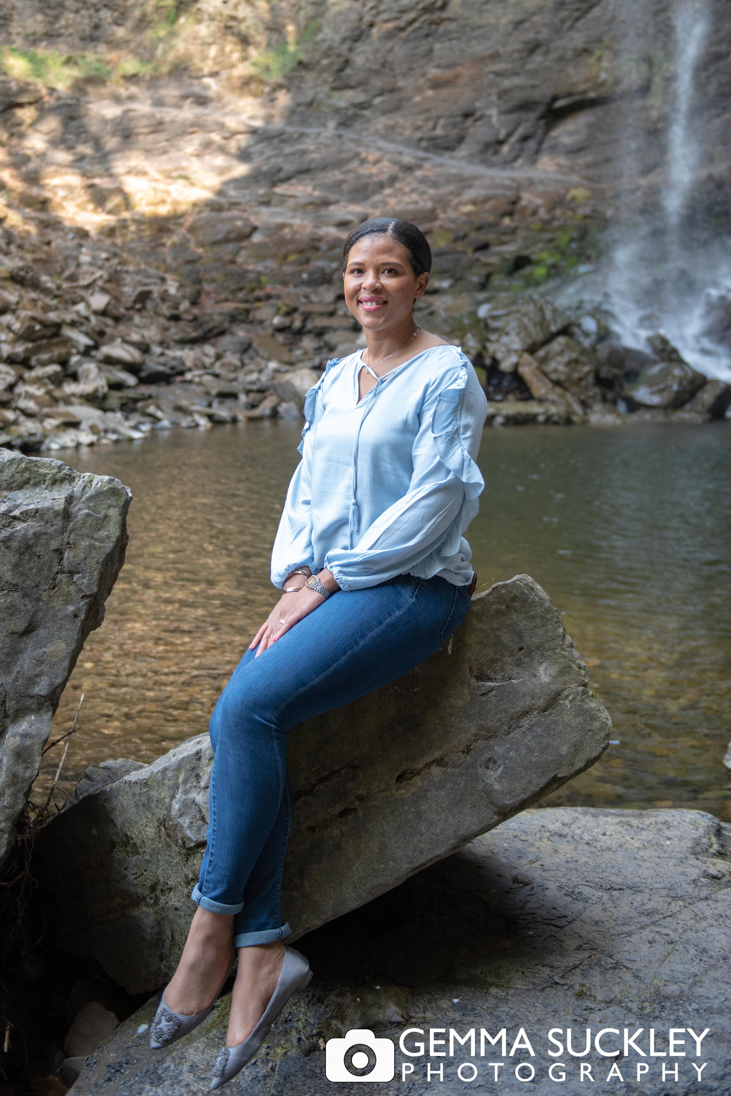 profession photo of a lady sat on a rock with hardraw force waterfall behind her