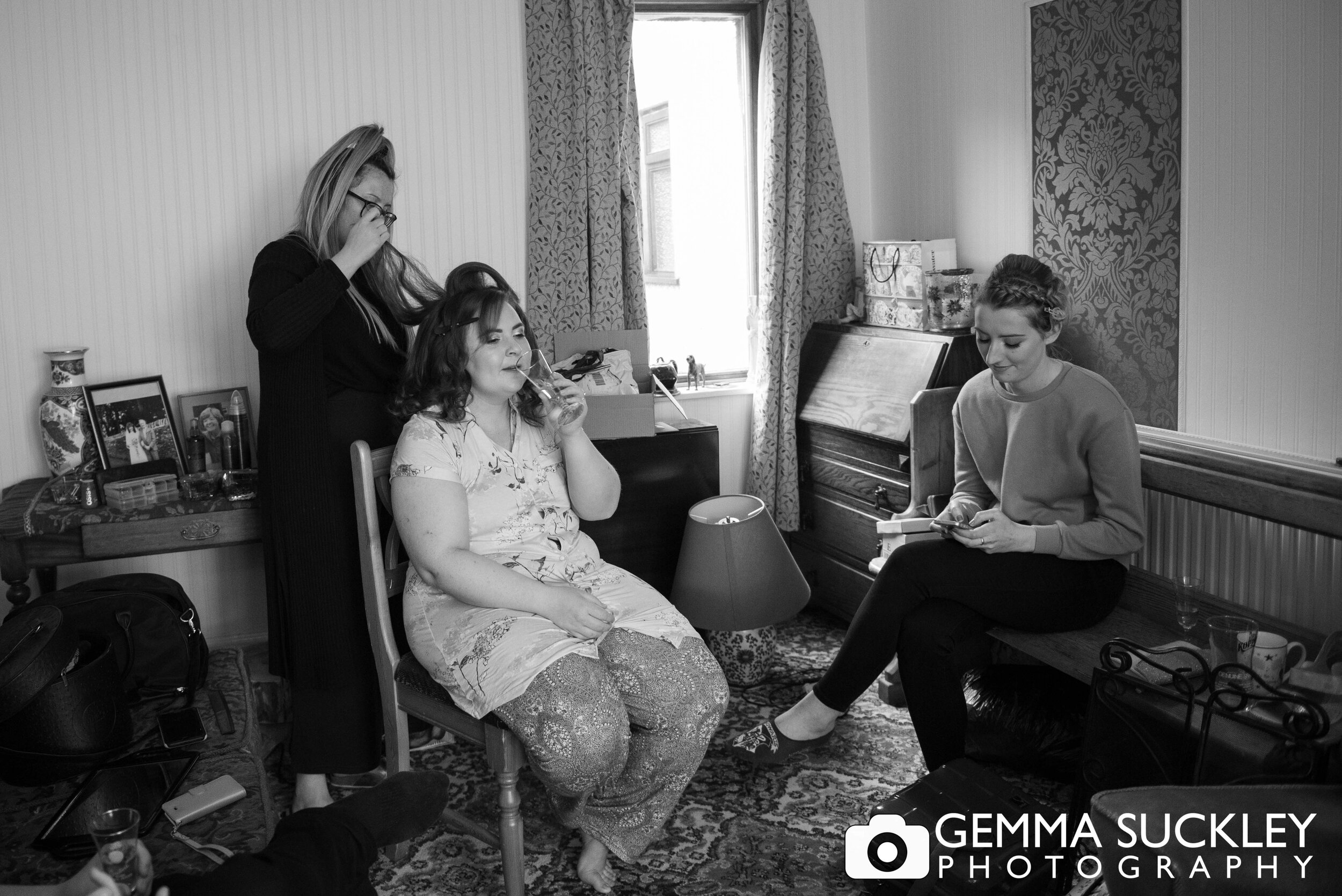 black and white photo of bride and bridesmaid getting hair done 