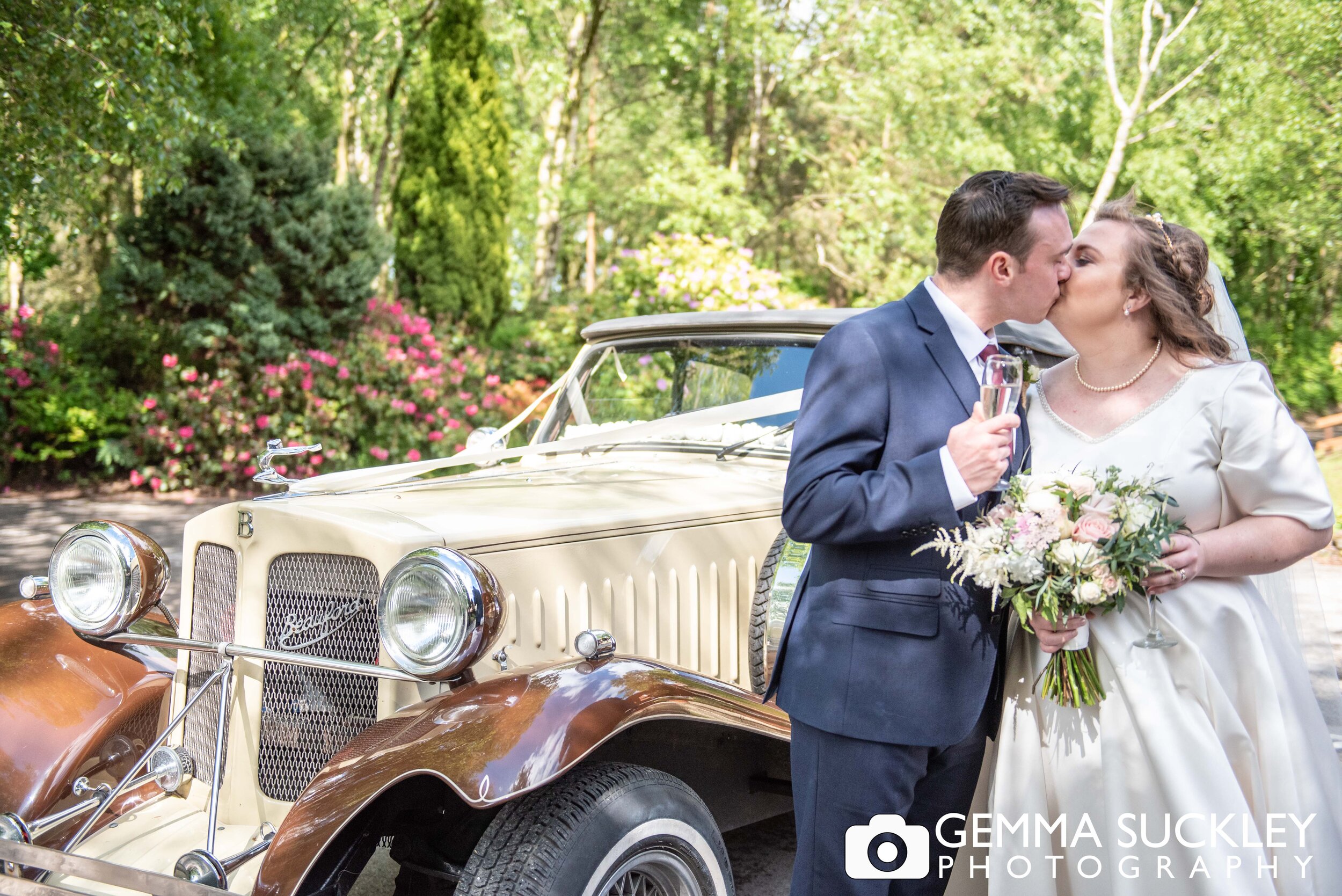 just married couple kissing in front of their vintage wedding car