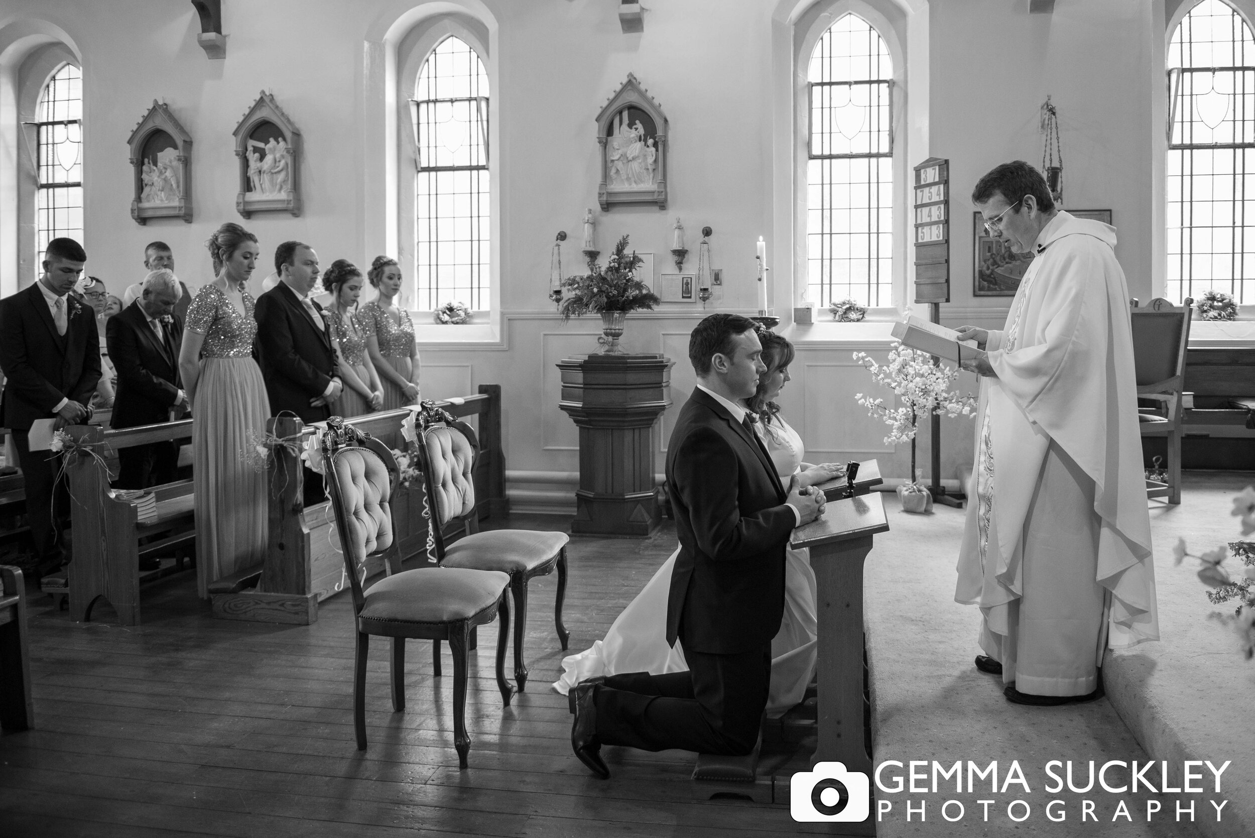 black and white wedding photography of the vicar blessing the bride and groom
