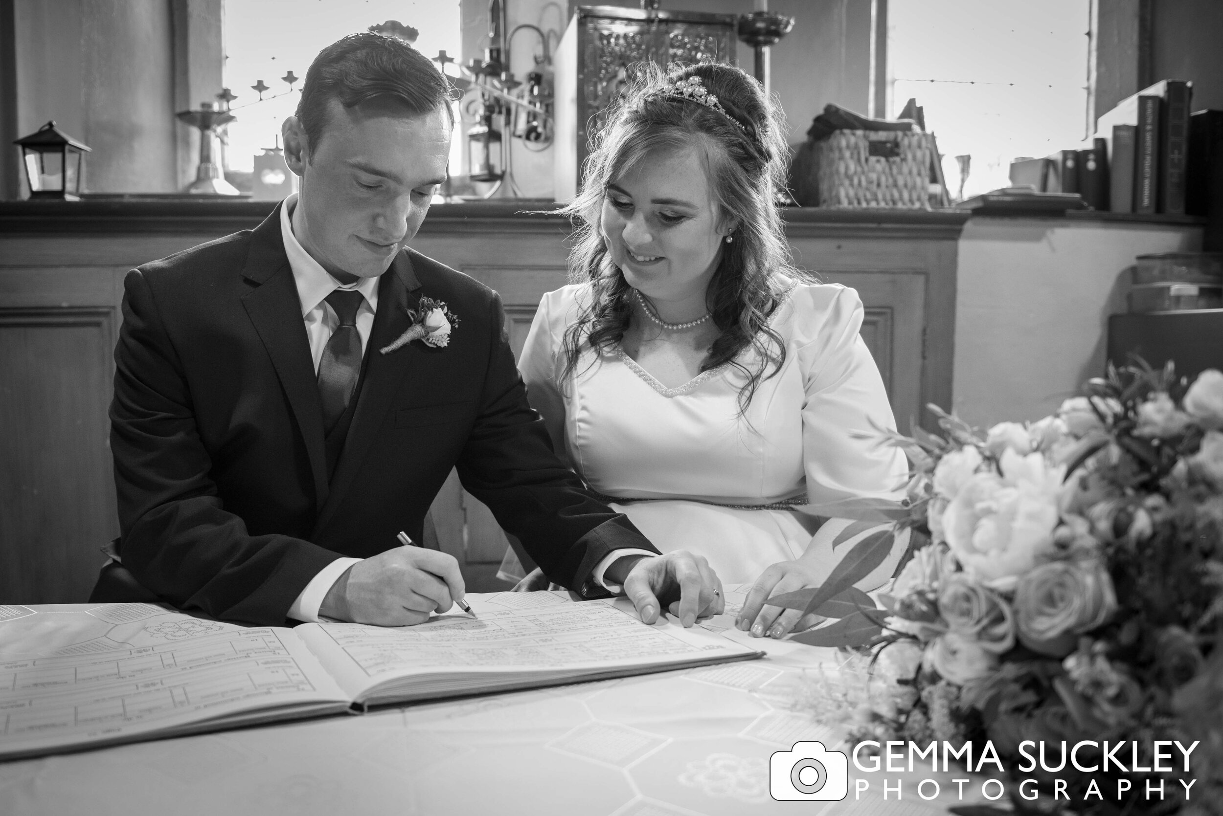 black and white wedding photo of bride and groom signing wedding the register