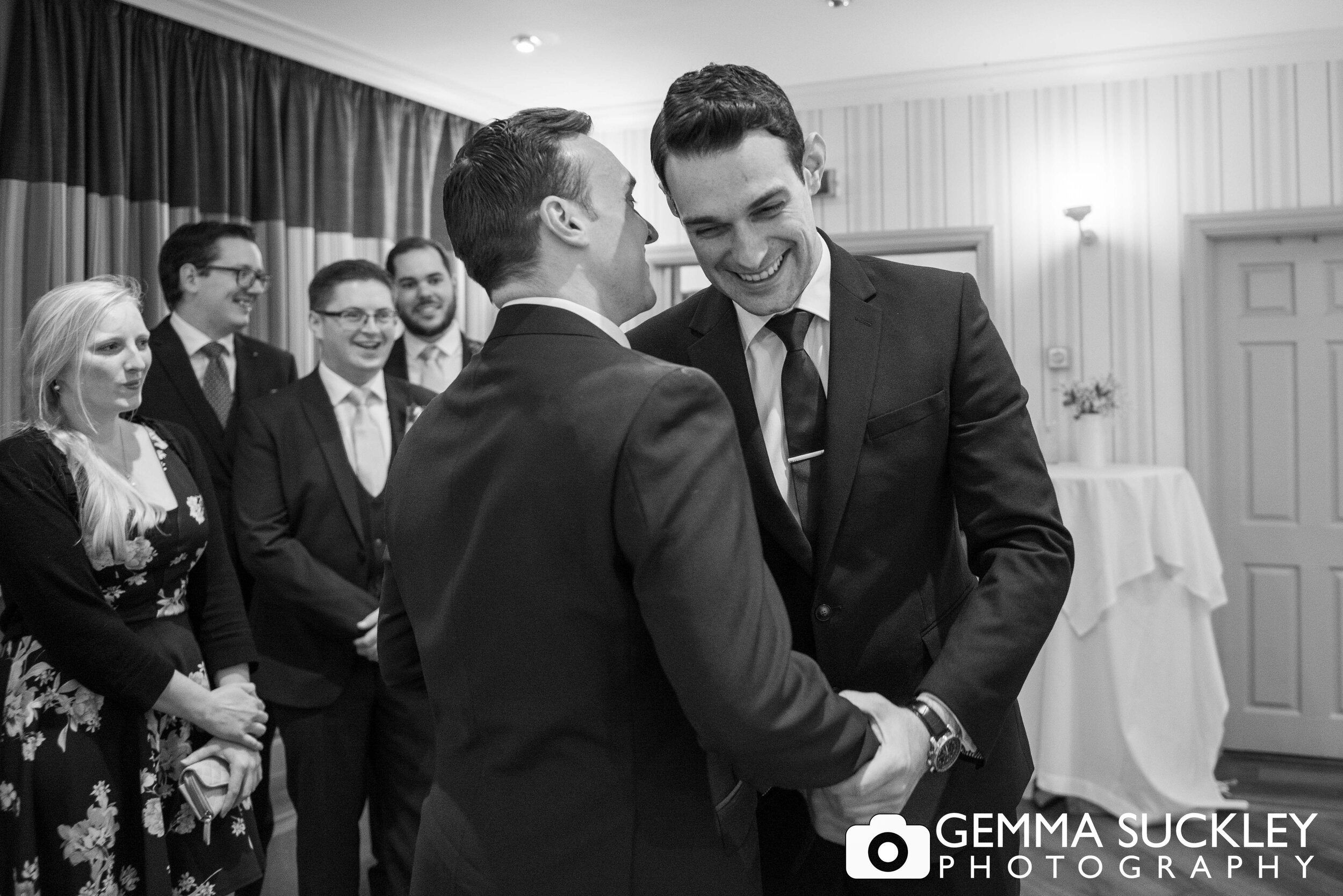 groom shaking hands with a guests while whispering in his ear, both are smiling