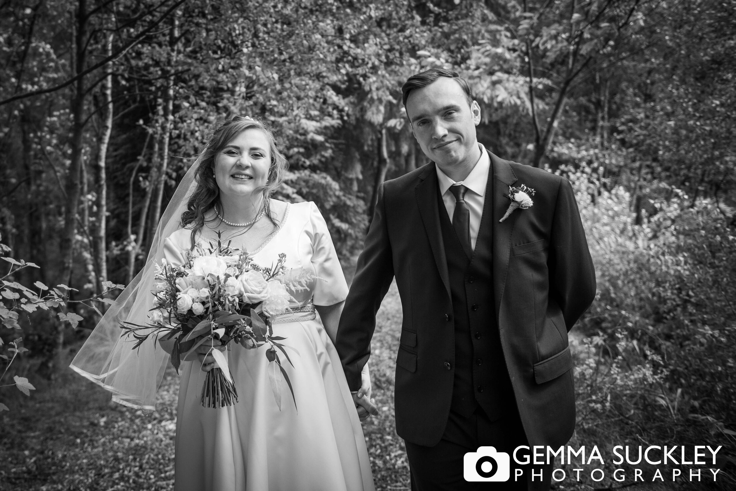 black and white wedding photo of the bride and groom walk through the trees at chevin country parkt 