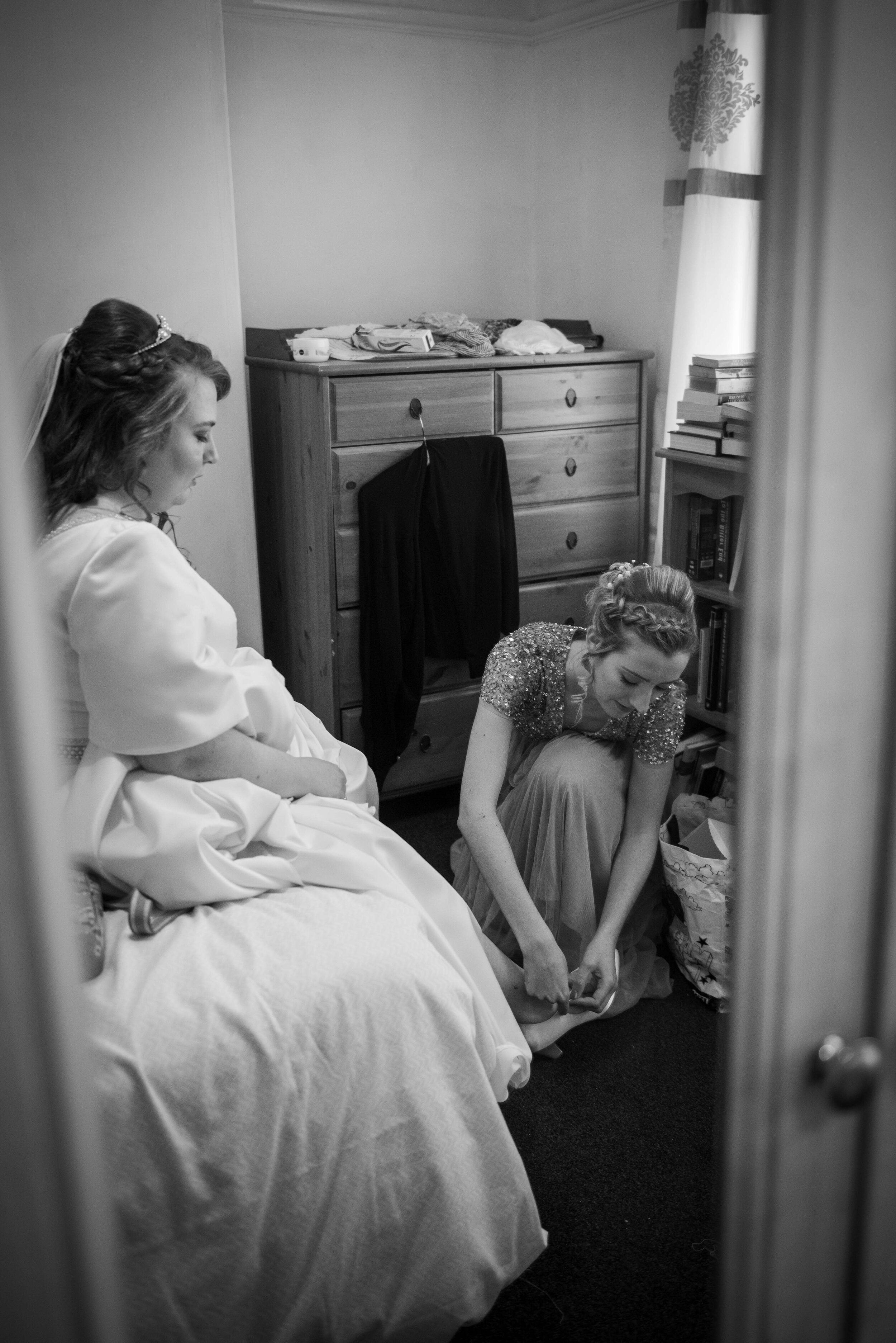 bridesmaid putting the brides shoes on for her