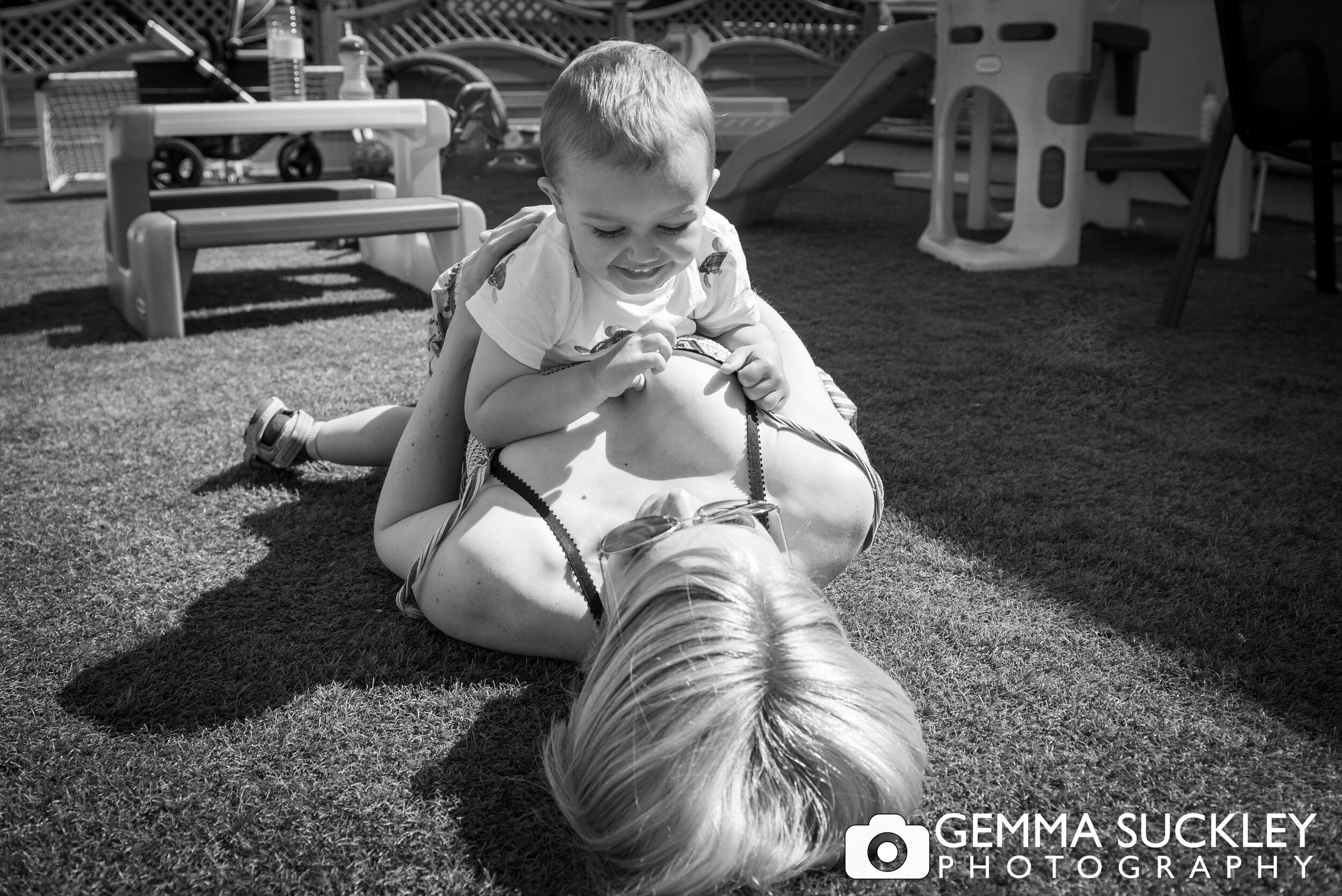 black and white photo of a little boy laying on his mum in the garden 