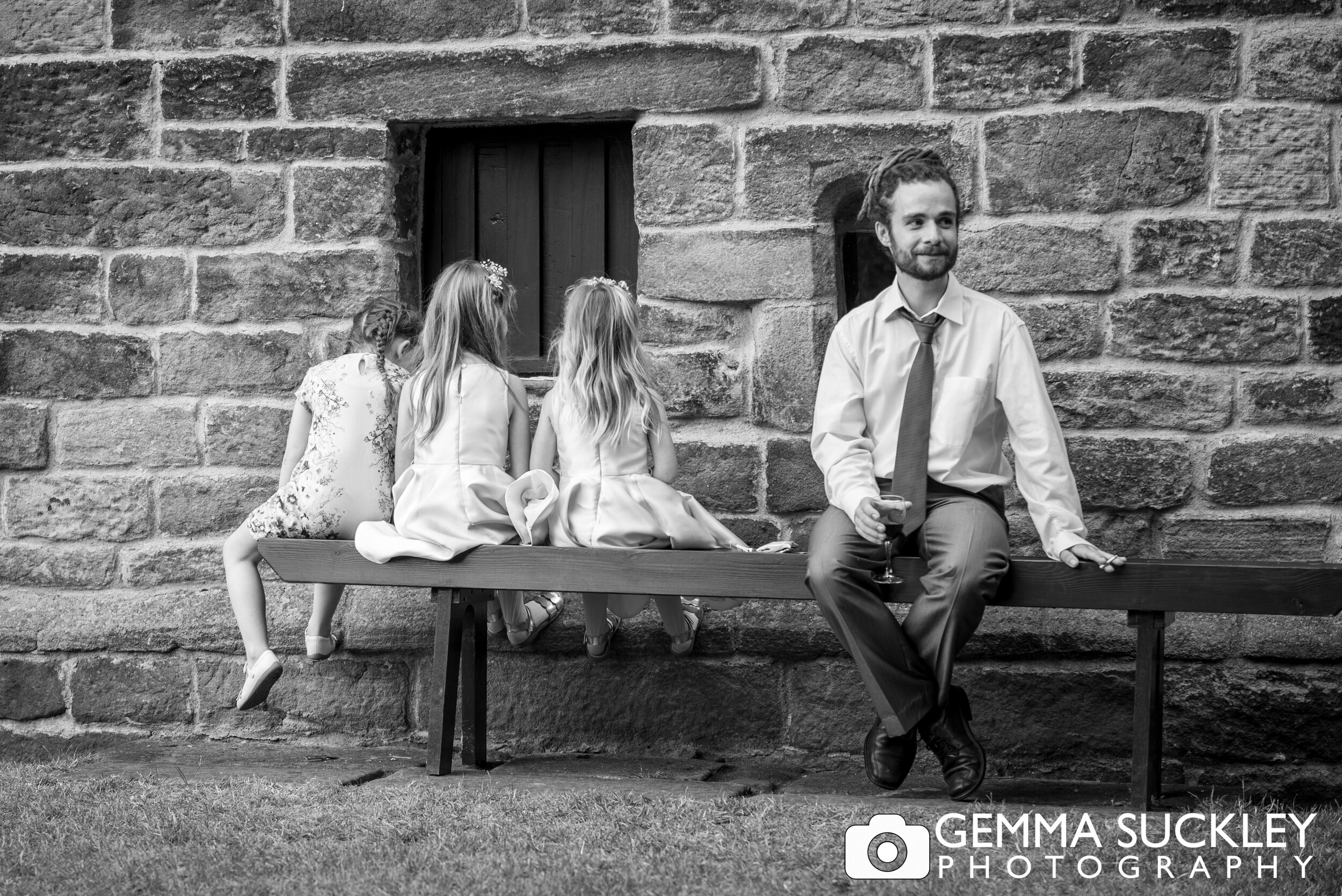 three children sitting the wrong way on a bench next to an uncomfortable looking wedding guest