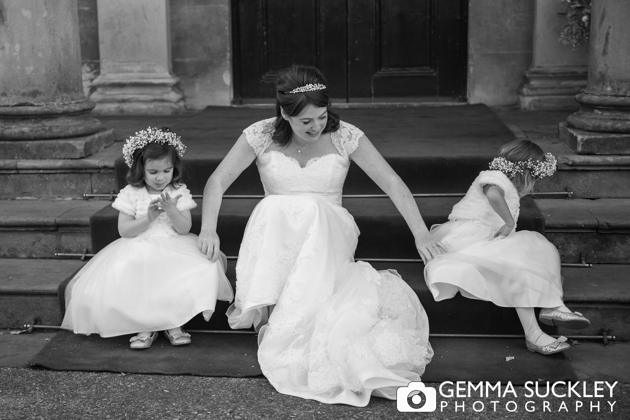 bride with two misbehaving flower girls sitting on a step 