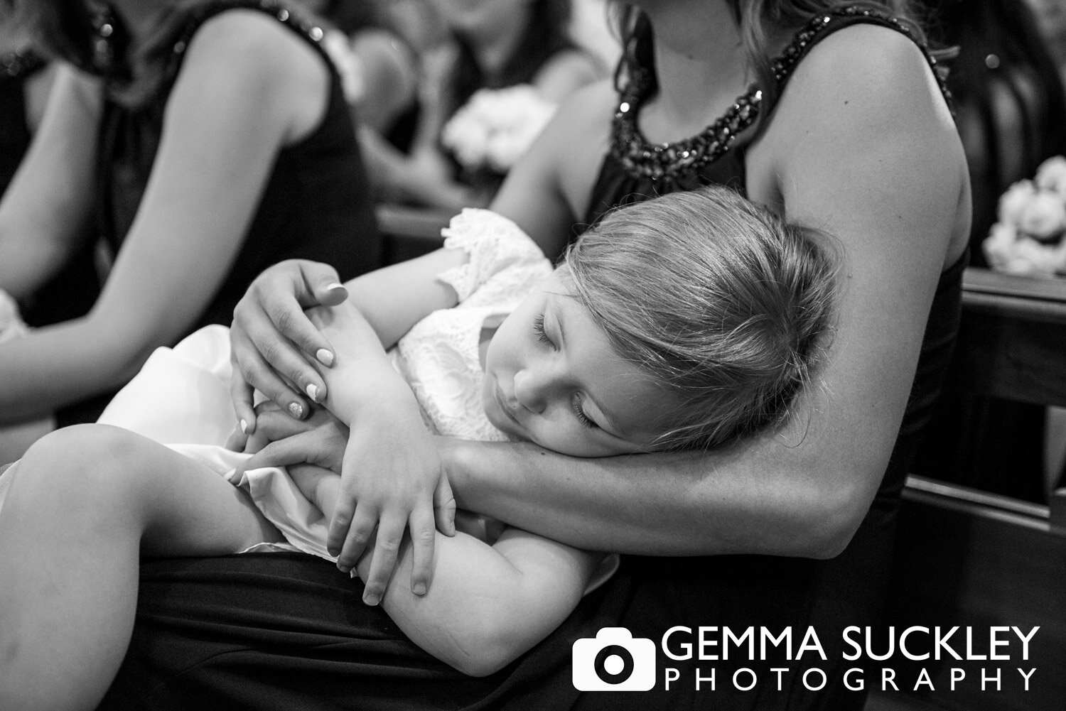 a flower girl asleep on her mums lap during the wedding ceremony