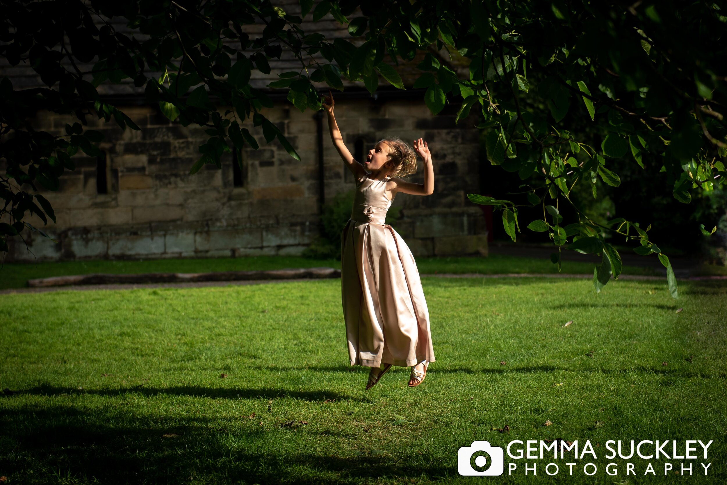 flower girl jumping to reach a tree branch at east riddlesden hall