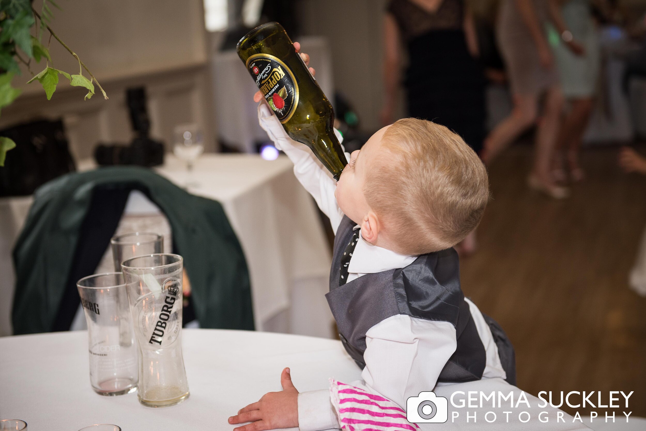 mischievous little boy drinking from a cider bottle at a wedding