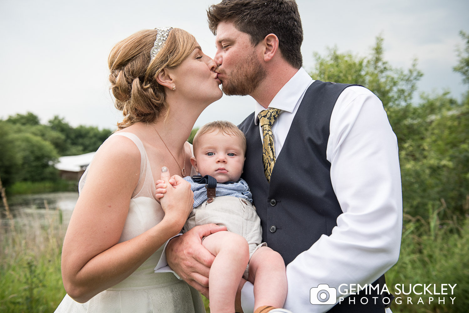 bride and groom kissing over the baby sons head