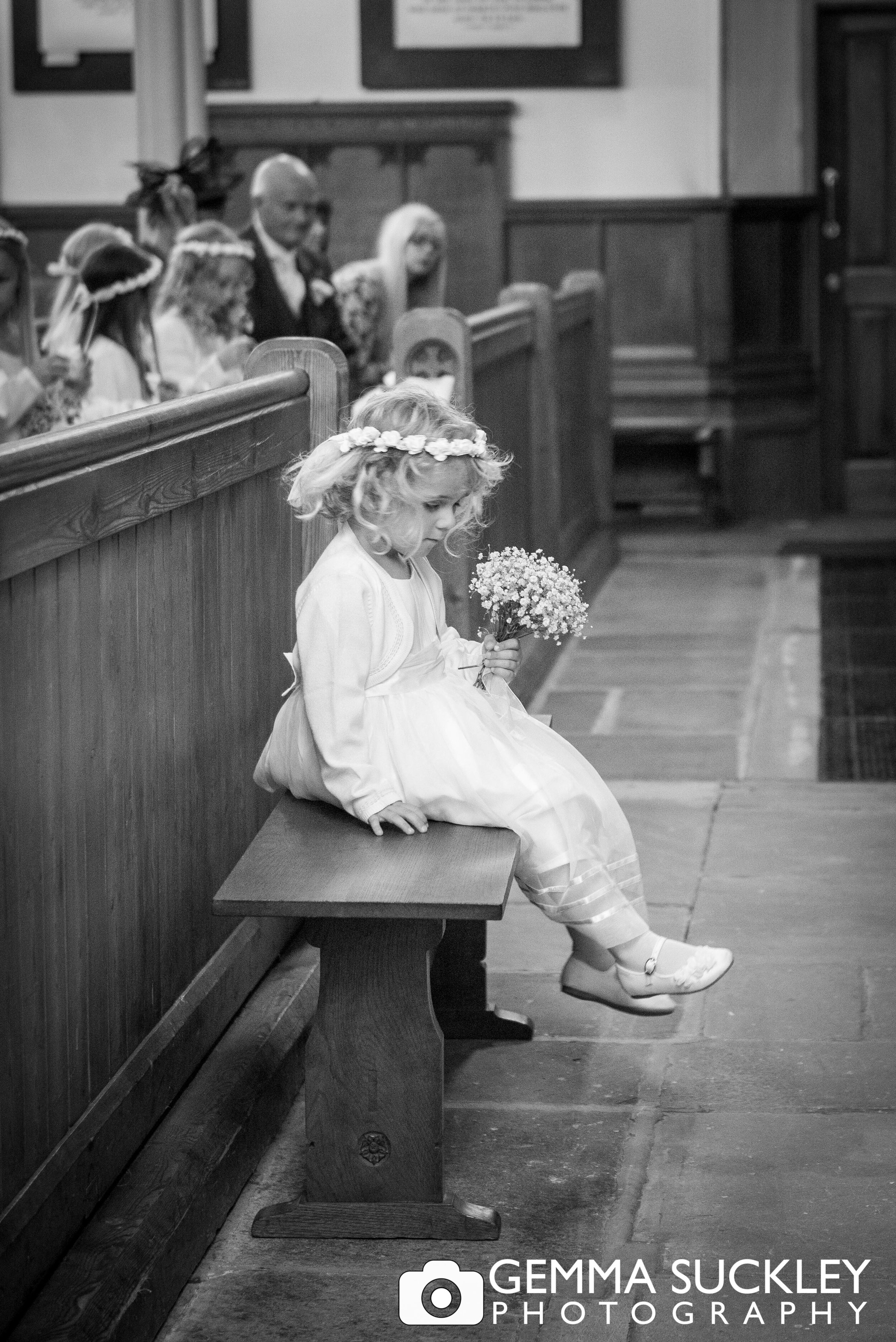 a little flower girl sat on a church pew alone 