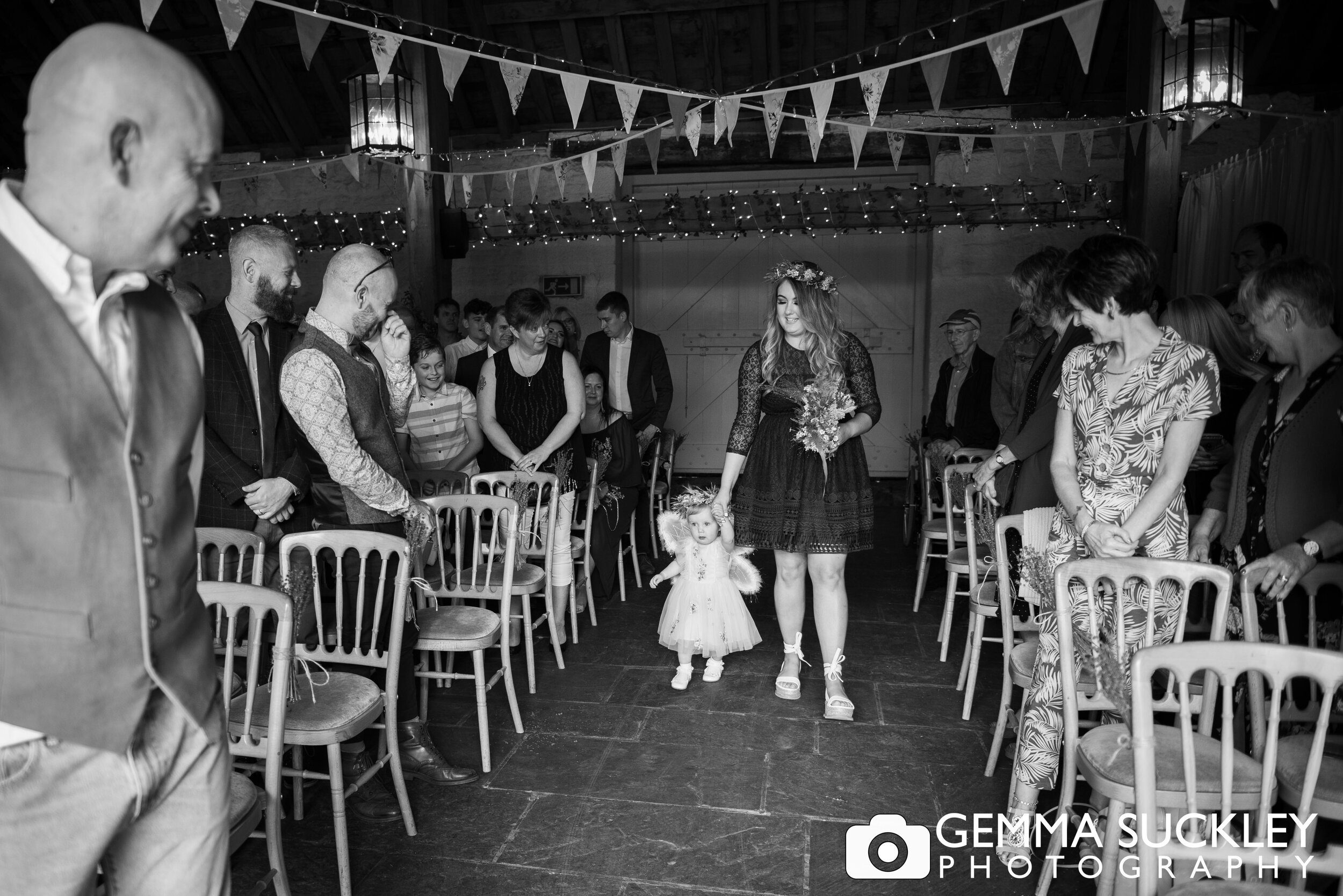 baby flower girl holding a bridesmaids hand walking down the aisle at east riddlesden hall