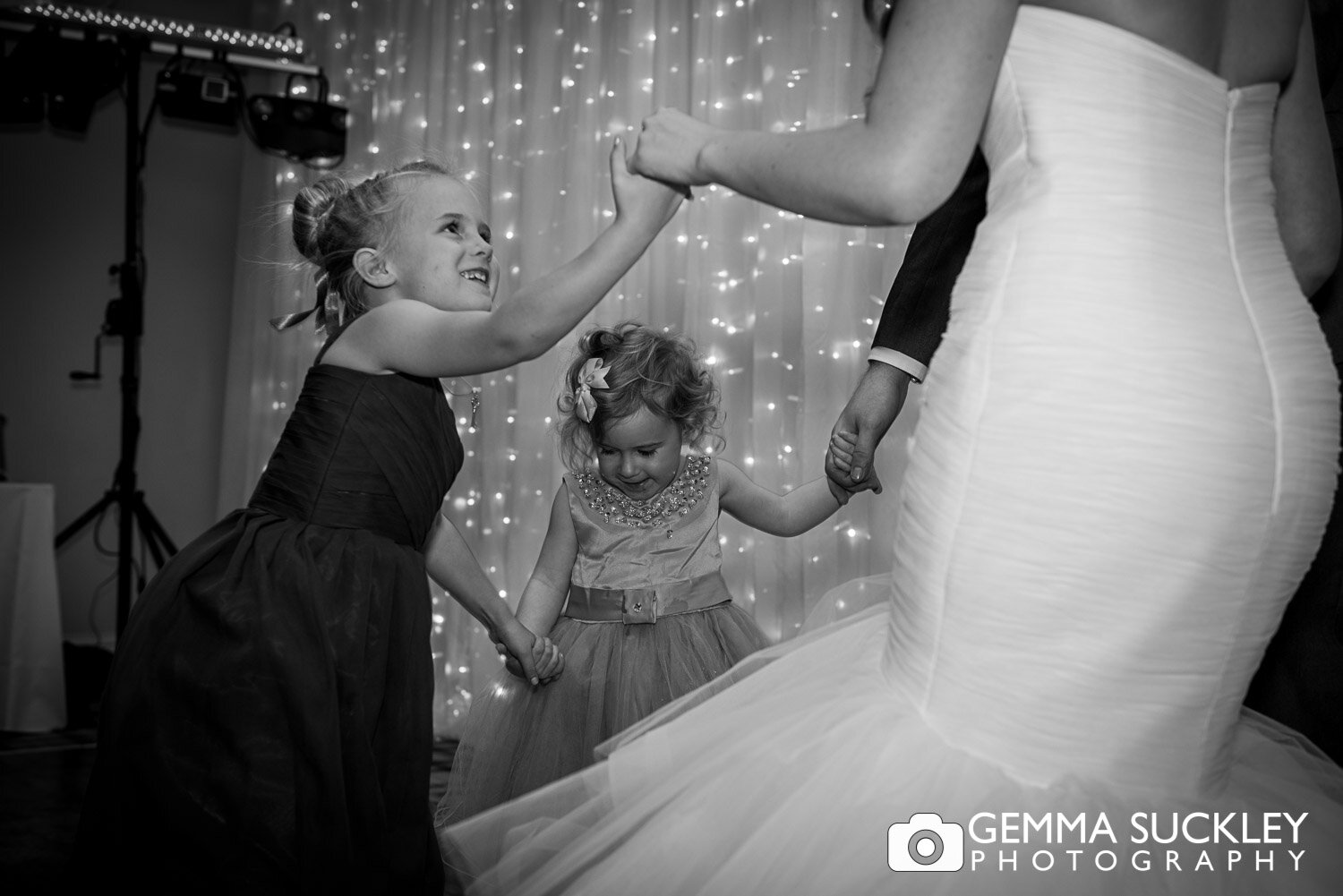 two flower girls holding hands with the bride on the dance floor 