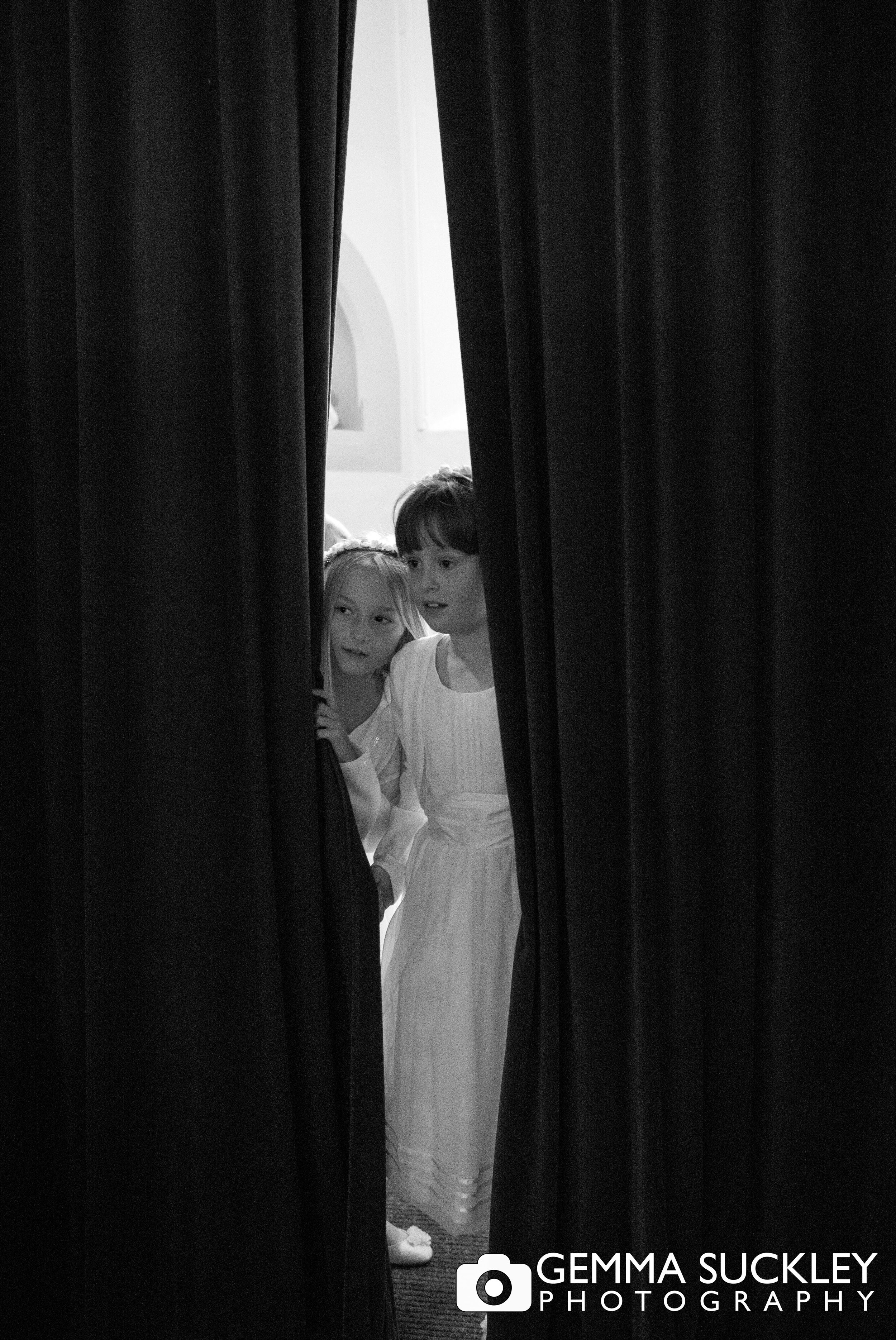 two flower girls peaking from being curtains at a wedding