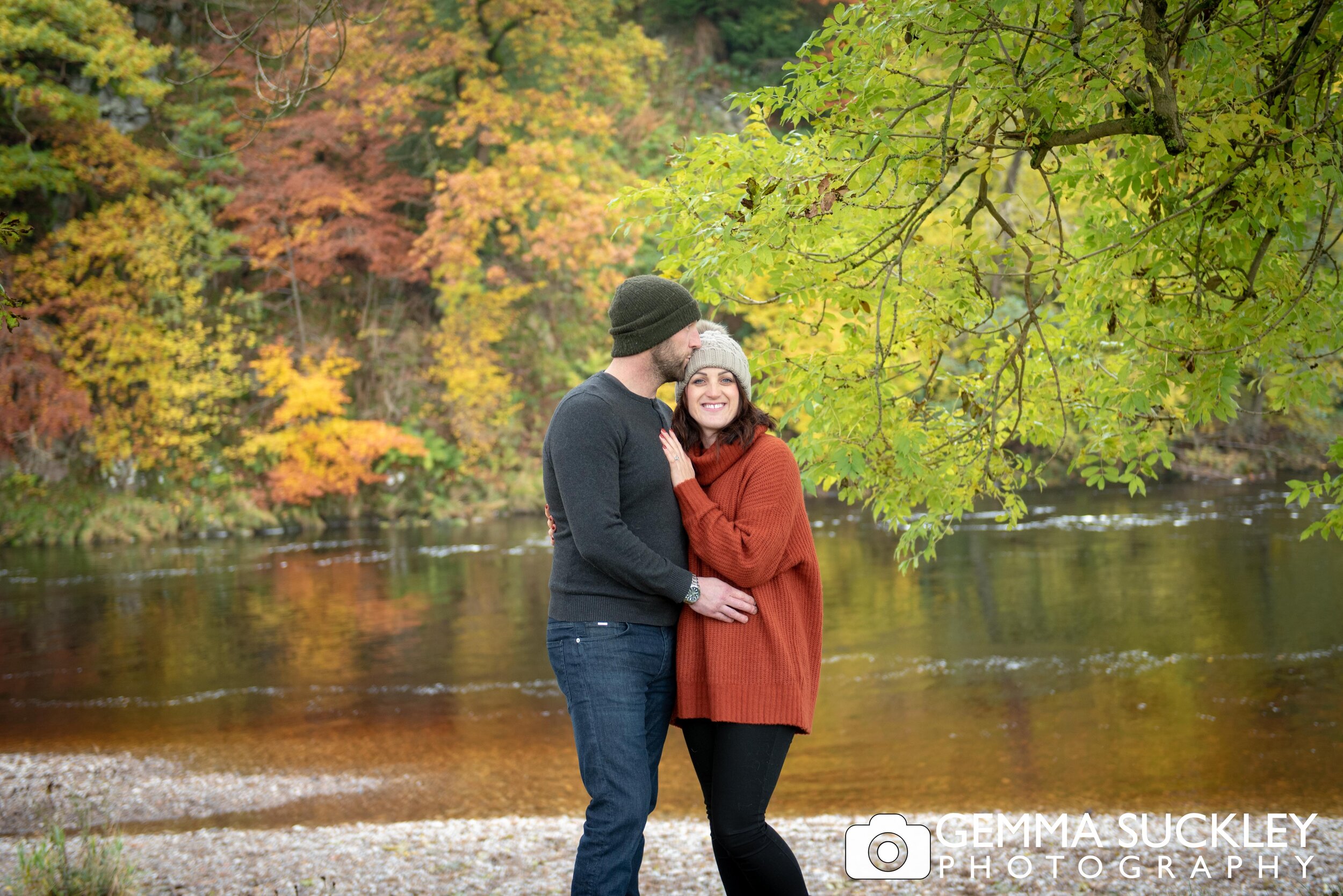 An engaged couple at bolton abbey with autumn trees behind them