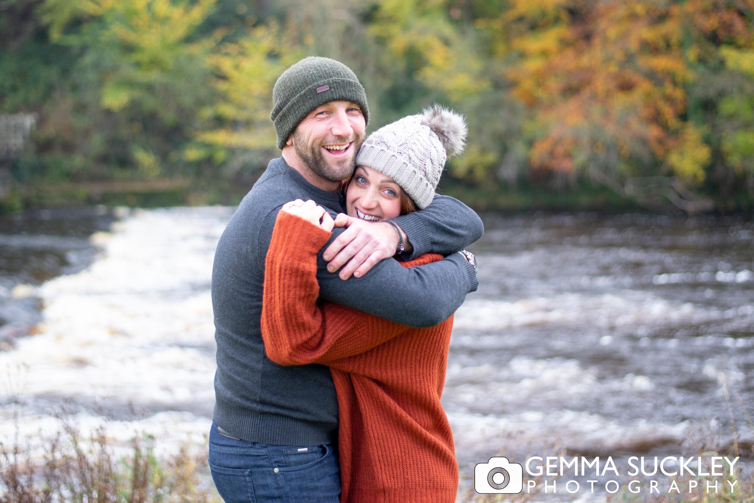 engagement photo of a hugging couple next to bolton abbey river