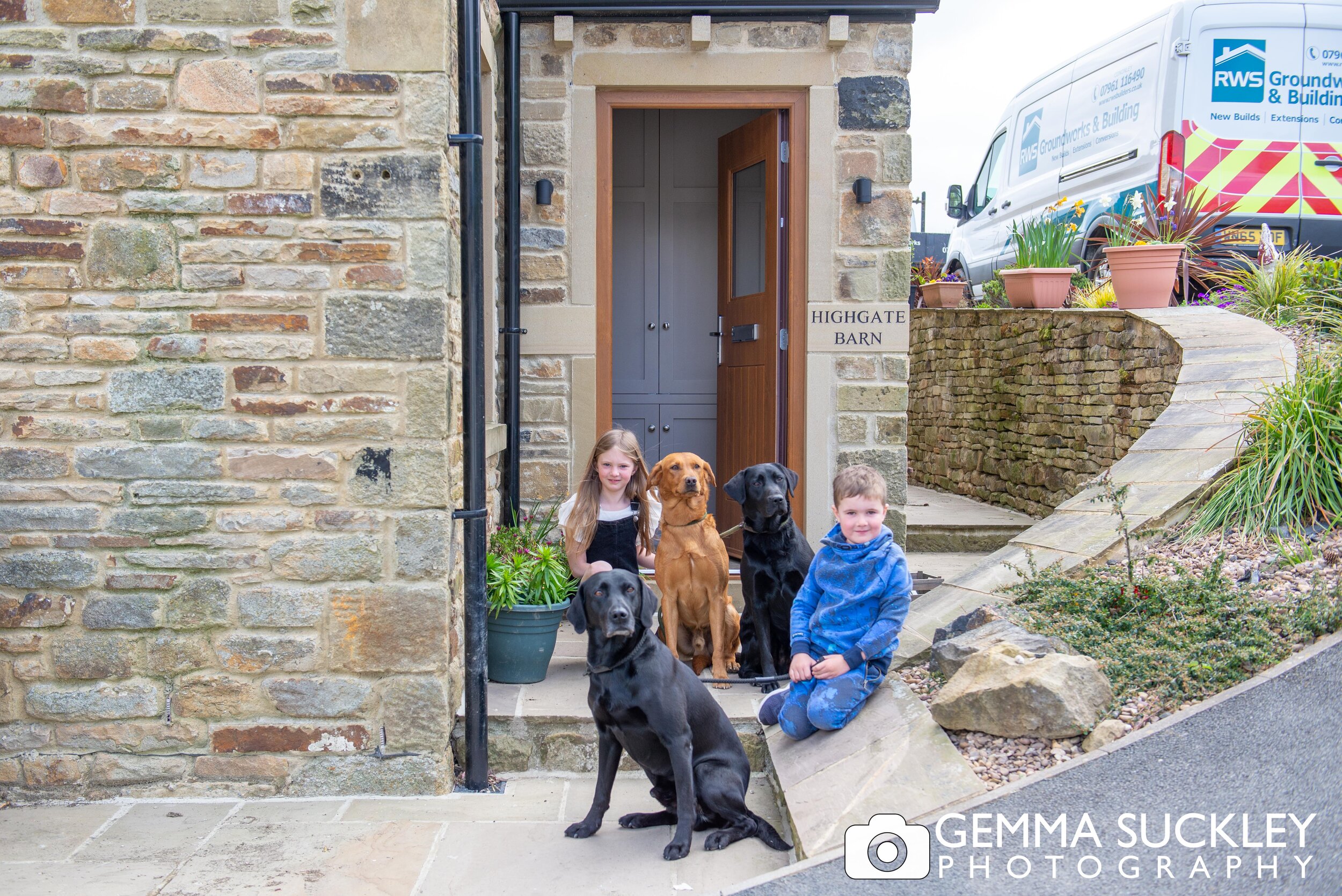 a doorstep photo of a young brother and sister with their 3  labrador dogs