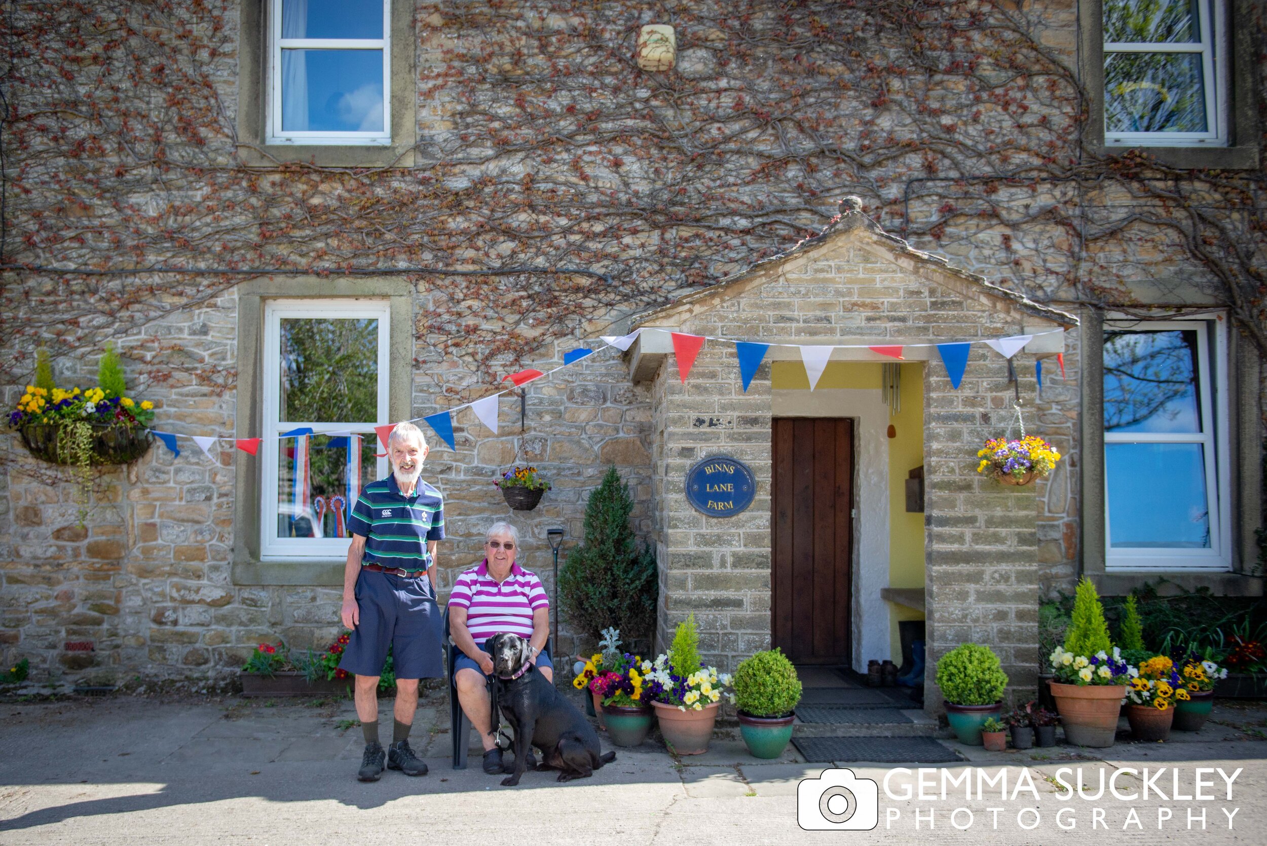 an elderly couple sitting outside their house smiling for a doorstep portrait