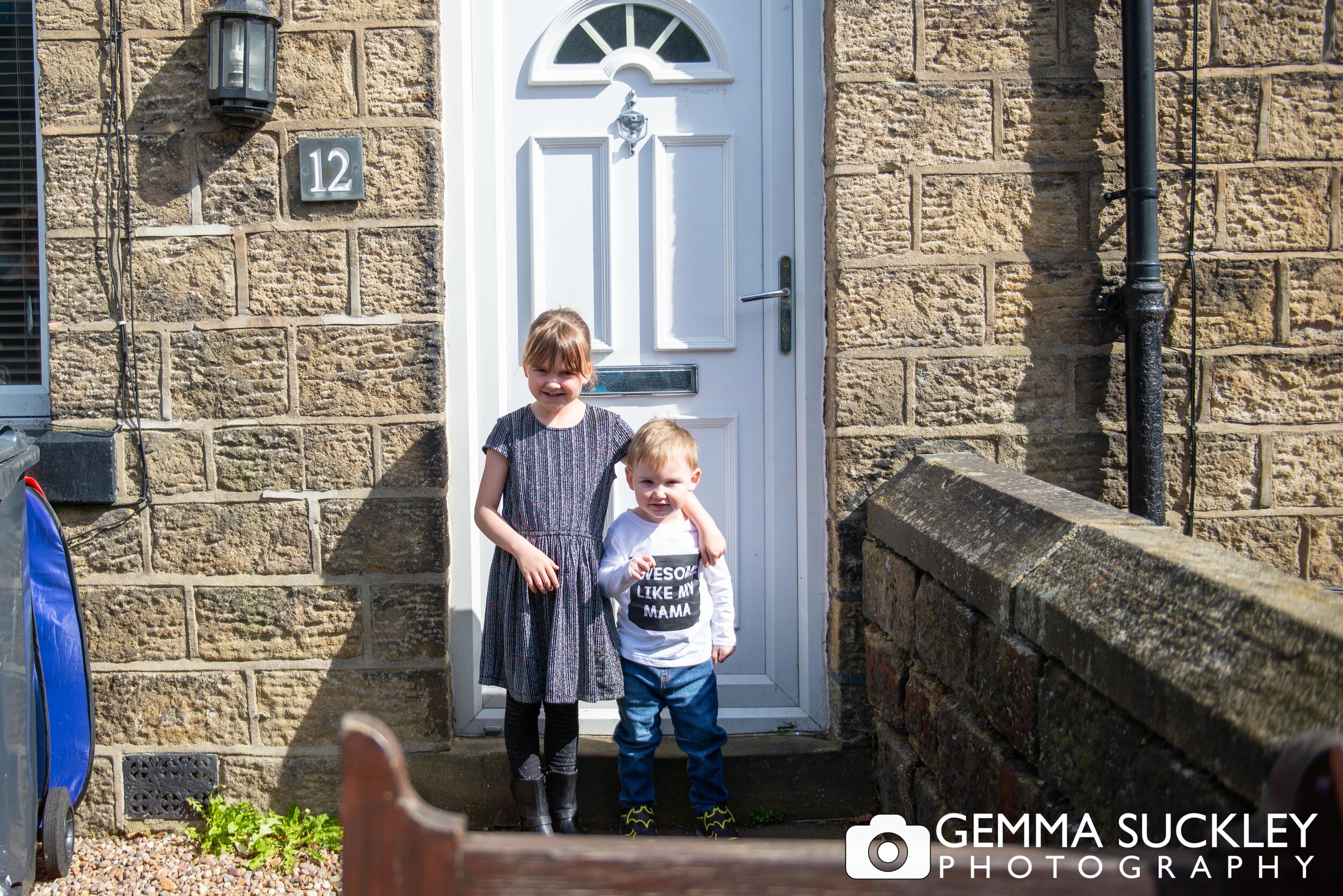 a young girl and her baby brother smiling for a doorstep photo in steeton