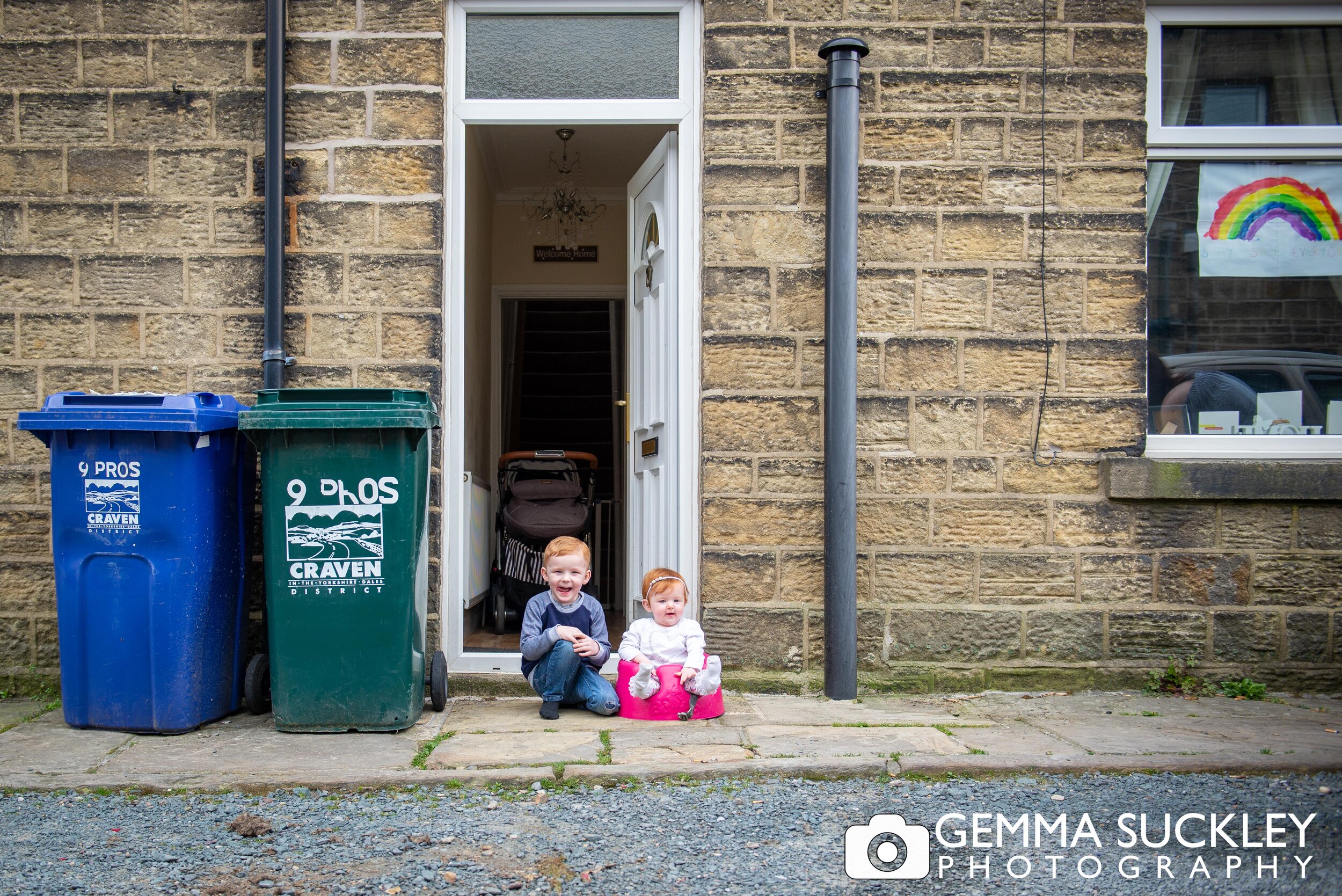 two young children sat outside the door with a rainbow painting in their window