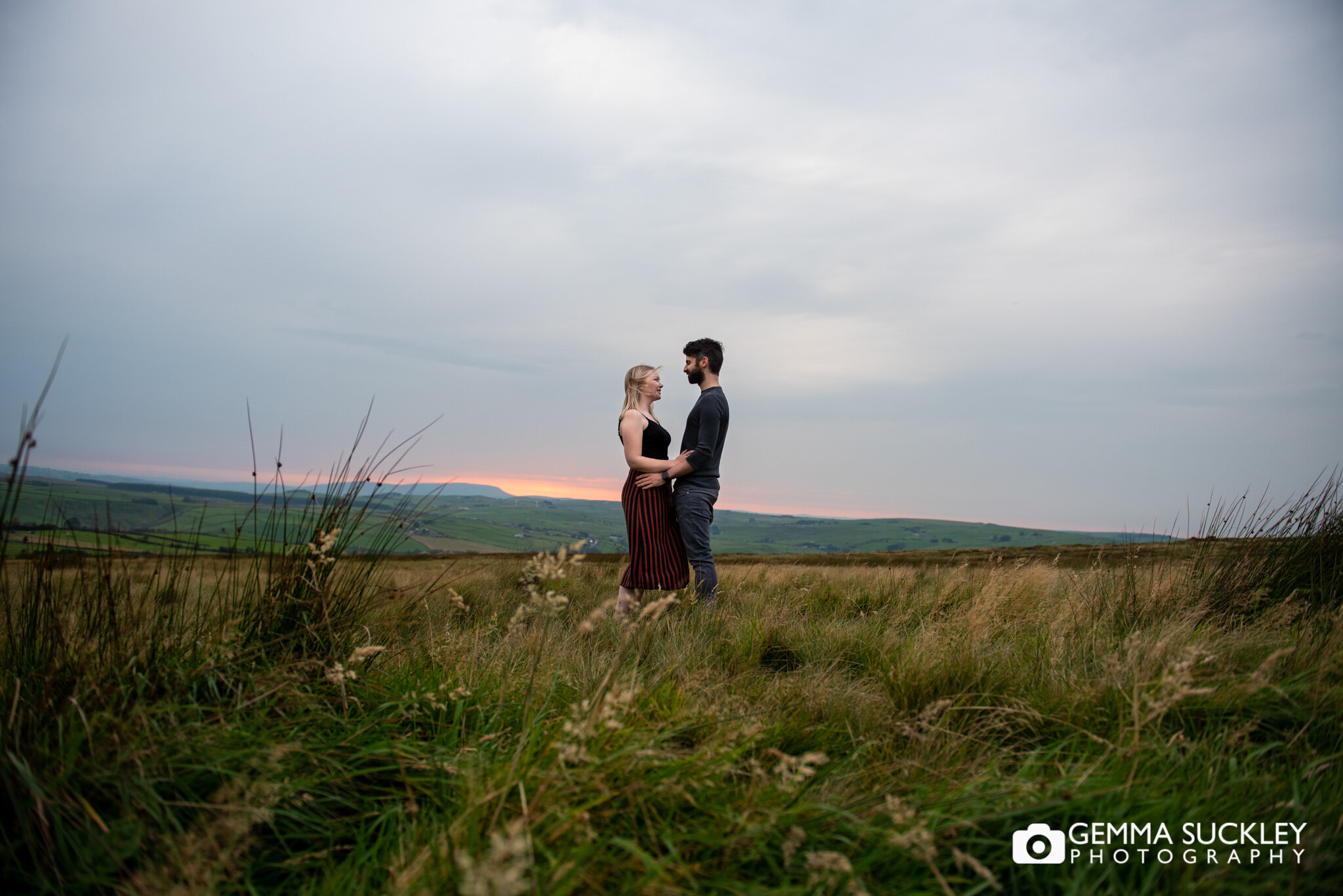 a couple hugging in a field with the sun setting behind them