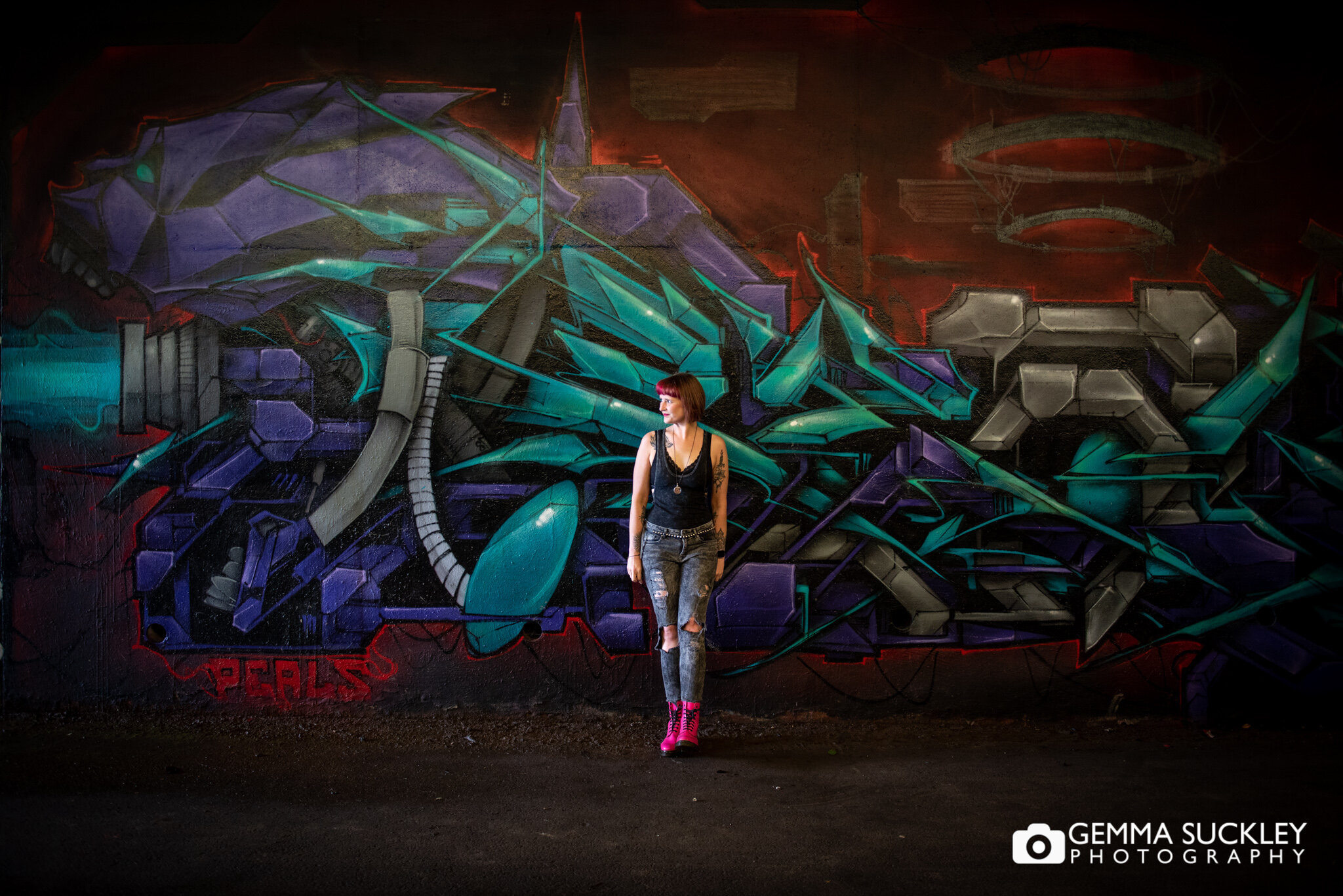 alternative looking girl smiling in front of a large graffitied wall