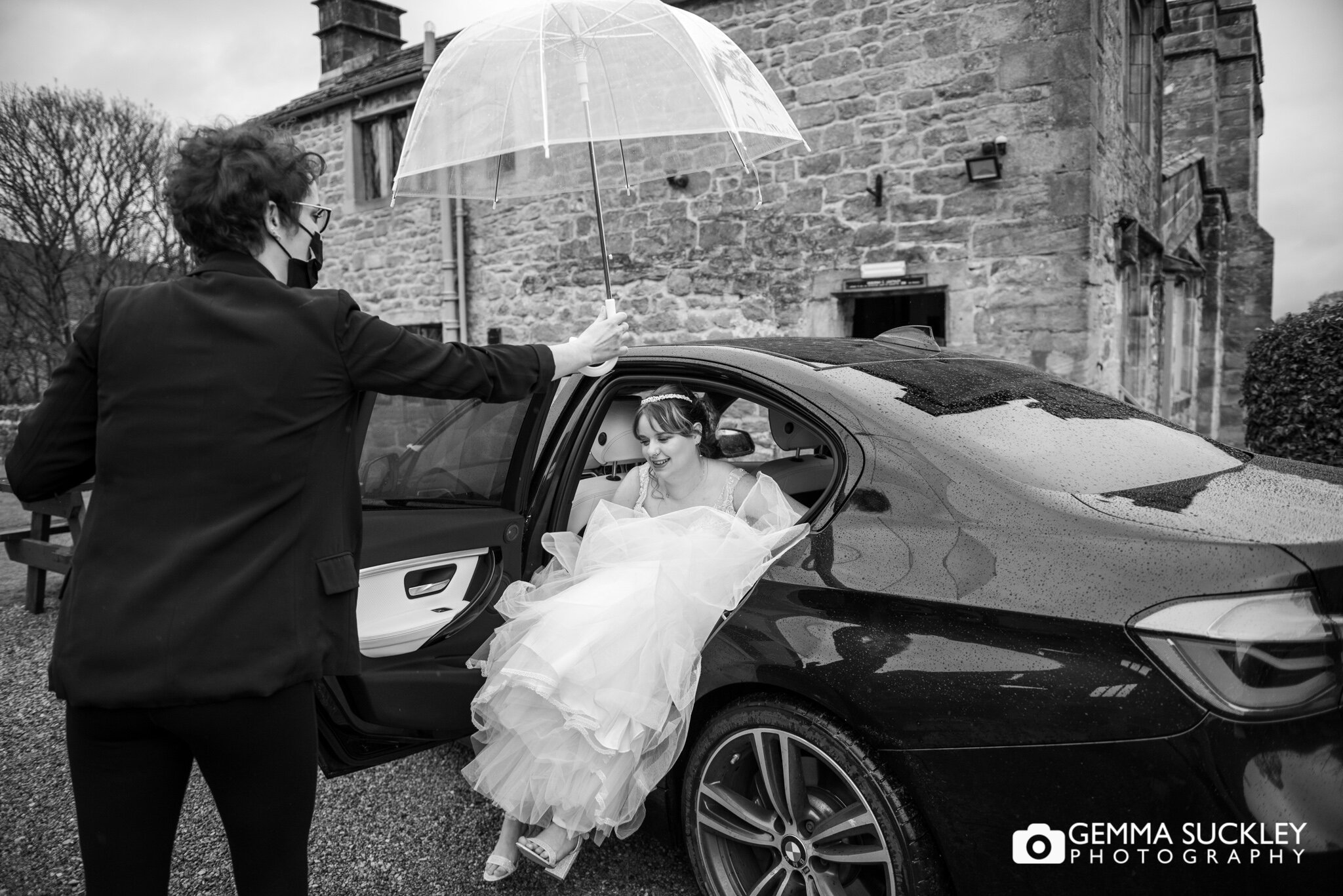 a  bride getting out the car with an umbrella held over her.