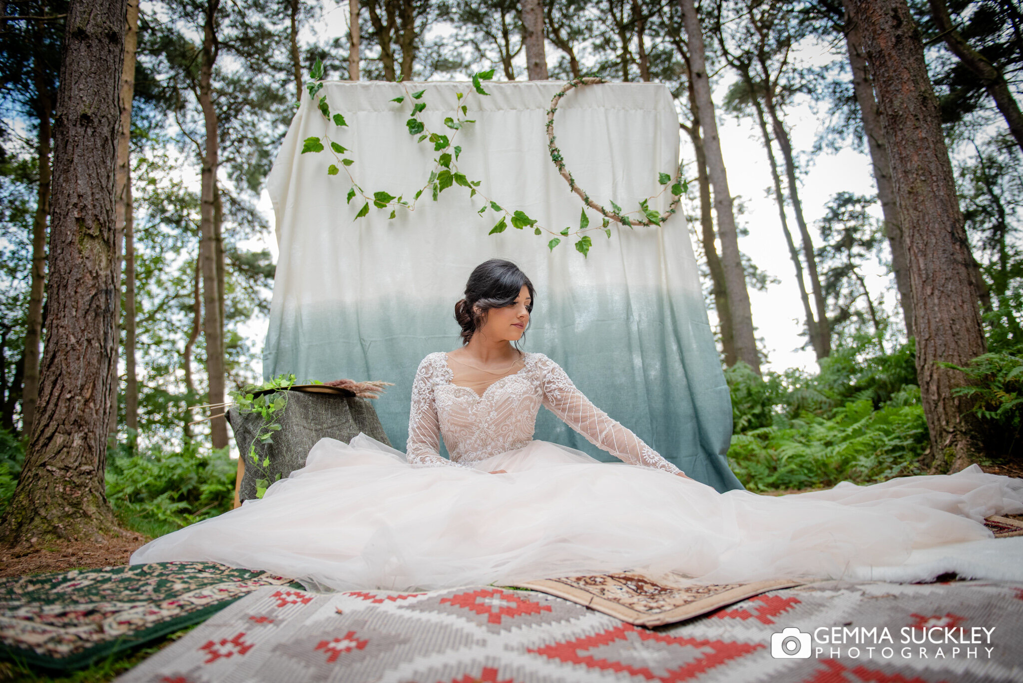 a bride sitting in the woods in front of a decorated backdrop