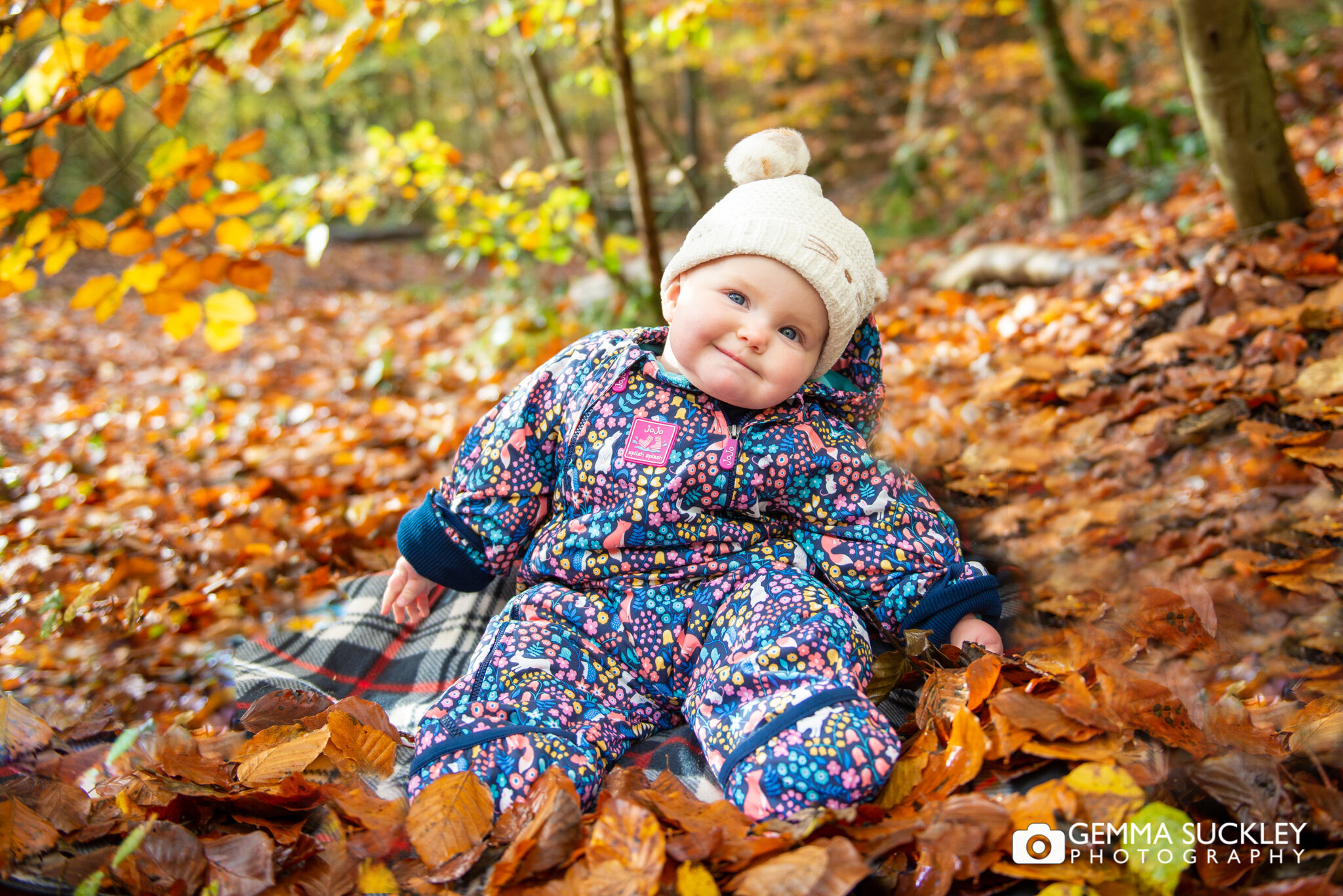 a smiling baby sitting in autumn leaves in skipton woods