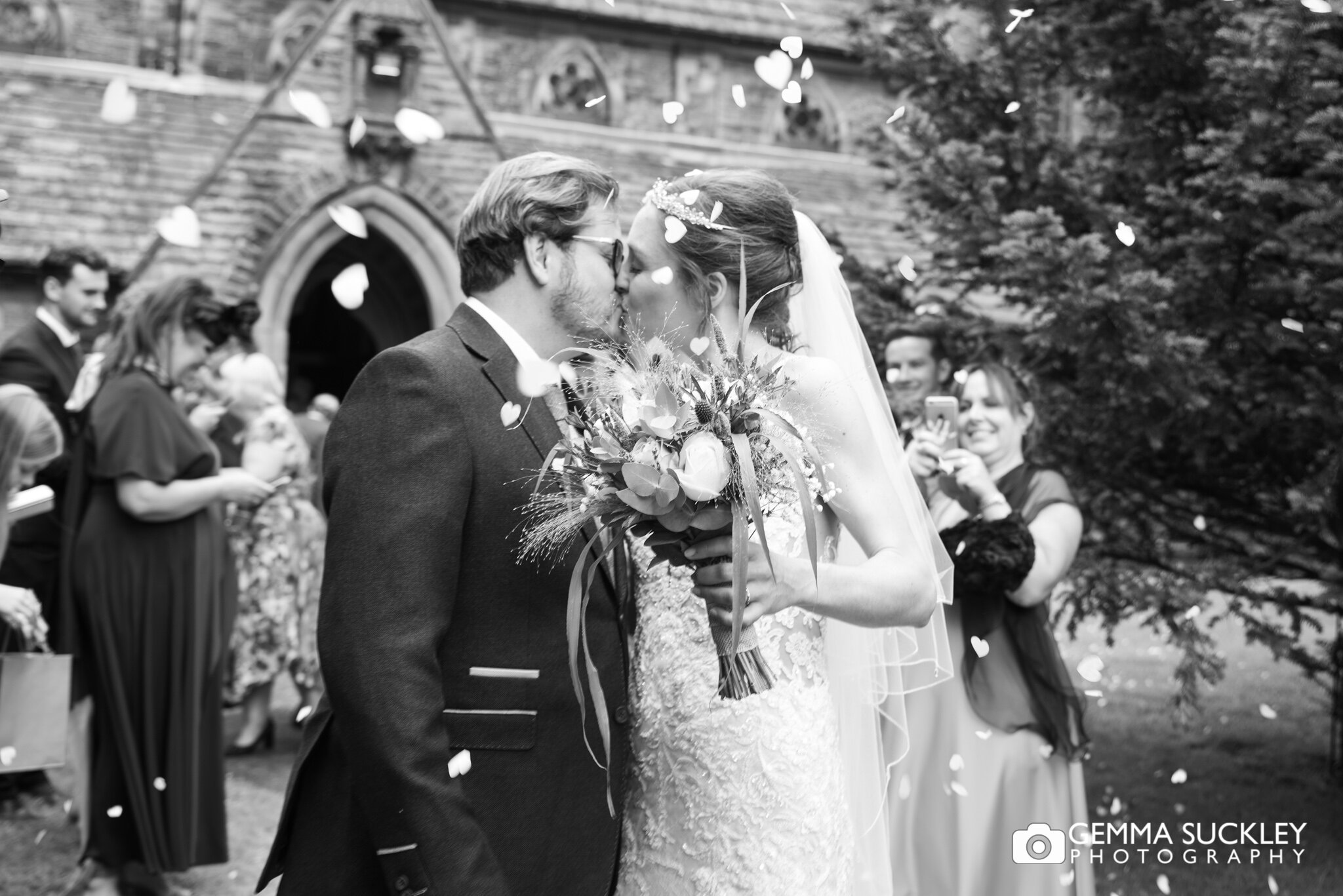 bride and groom kissing outside carleton church as guest throw confetti 
